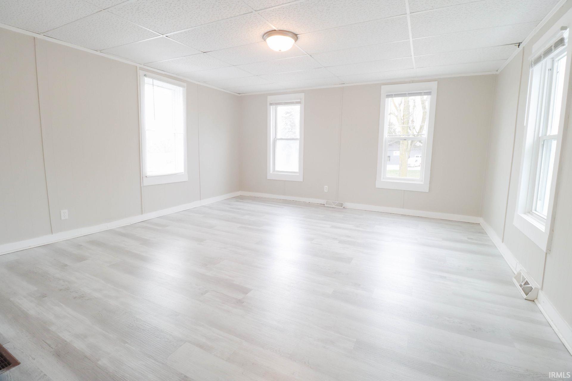 Empty room featuring healthy amount of natural light, a drop ceiling, and light wood-style flooring