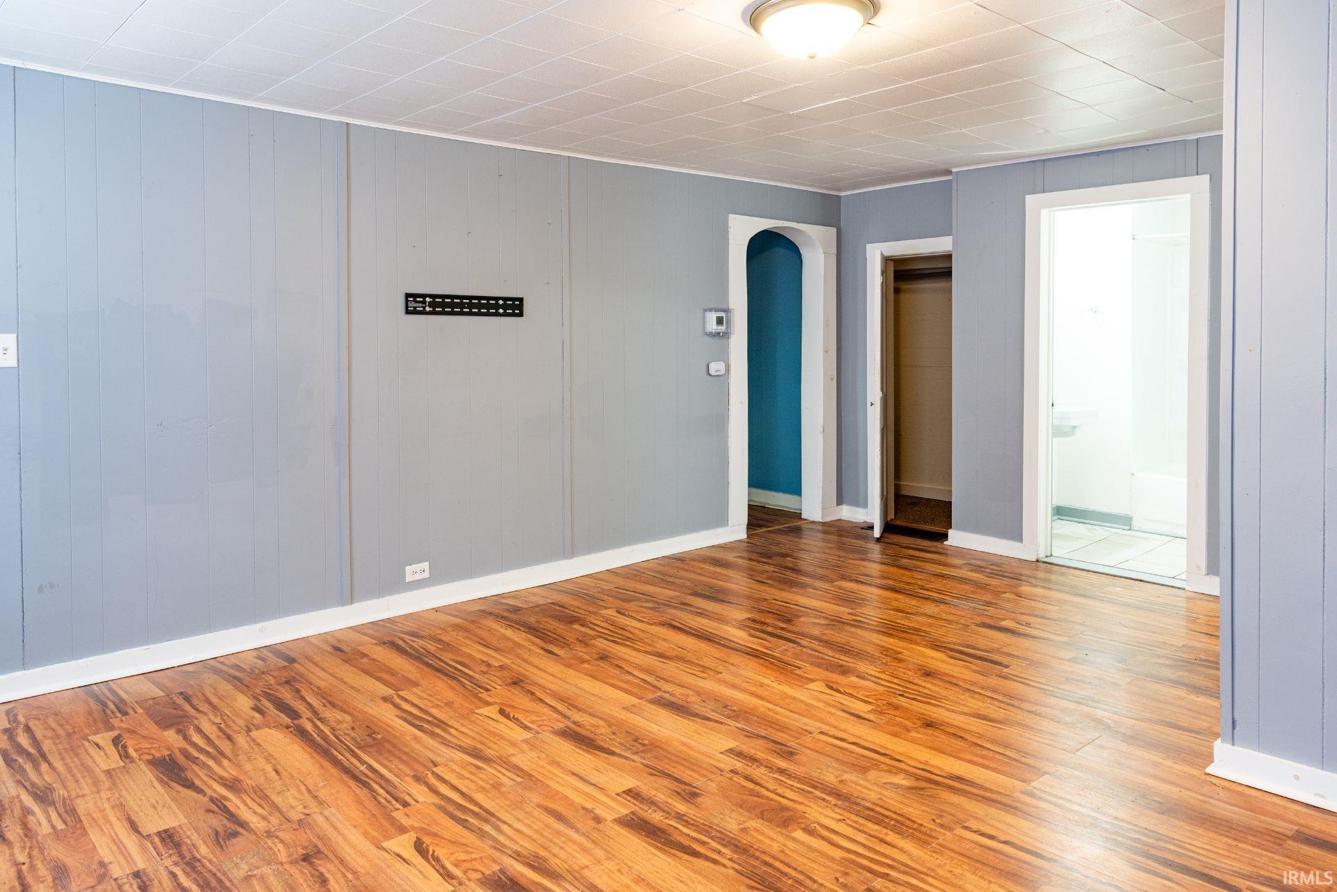 Empty room with arched walkways, wood finished floors, and wood walls