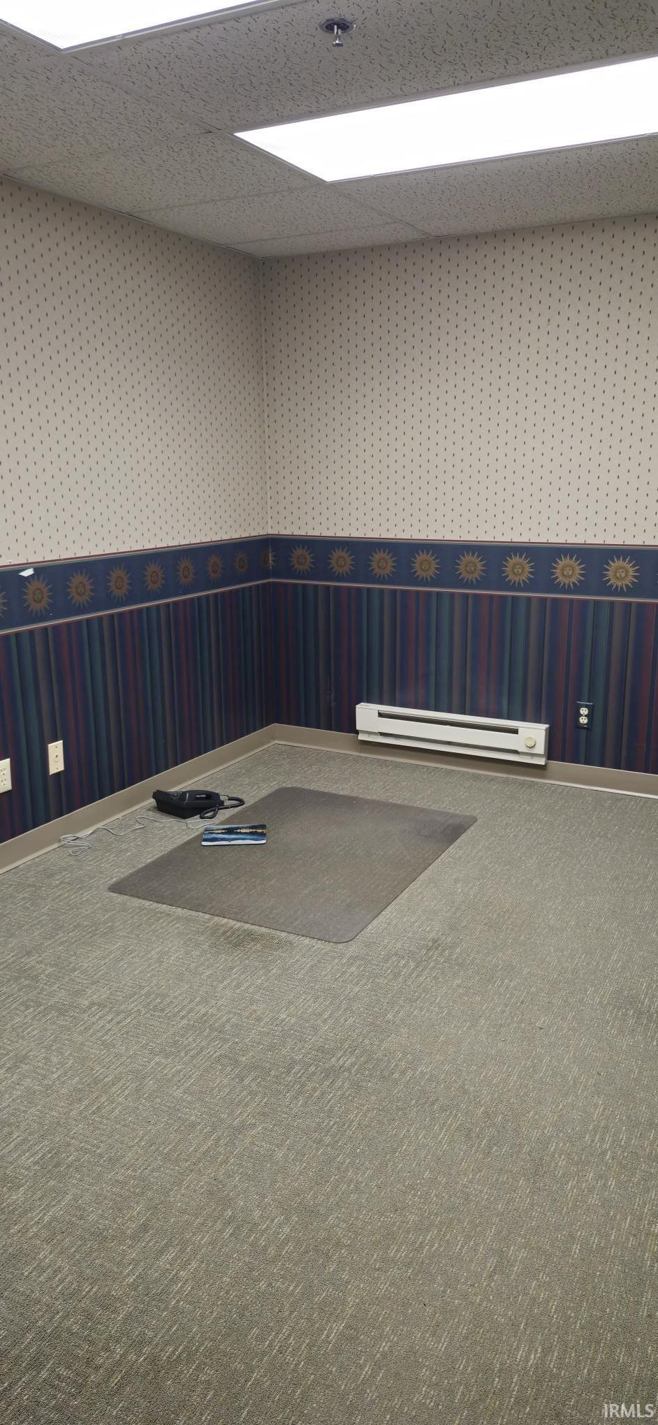 Unfurnished room featuring a wainscoted wall, wallpapered walls, carpet floors, a baseboard heating unit, and a drop ceiling