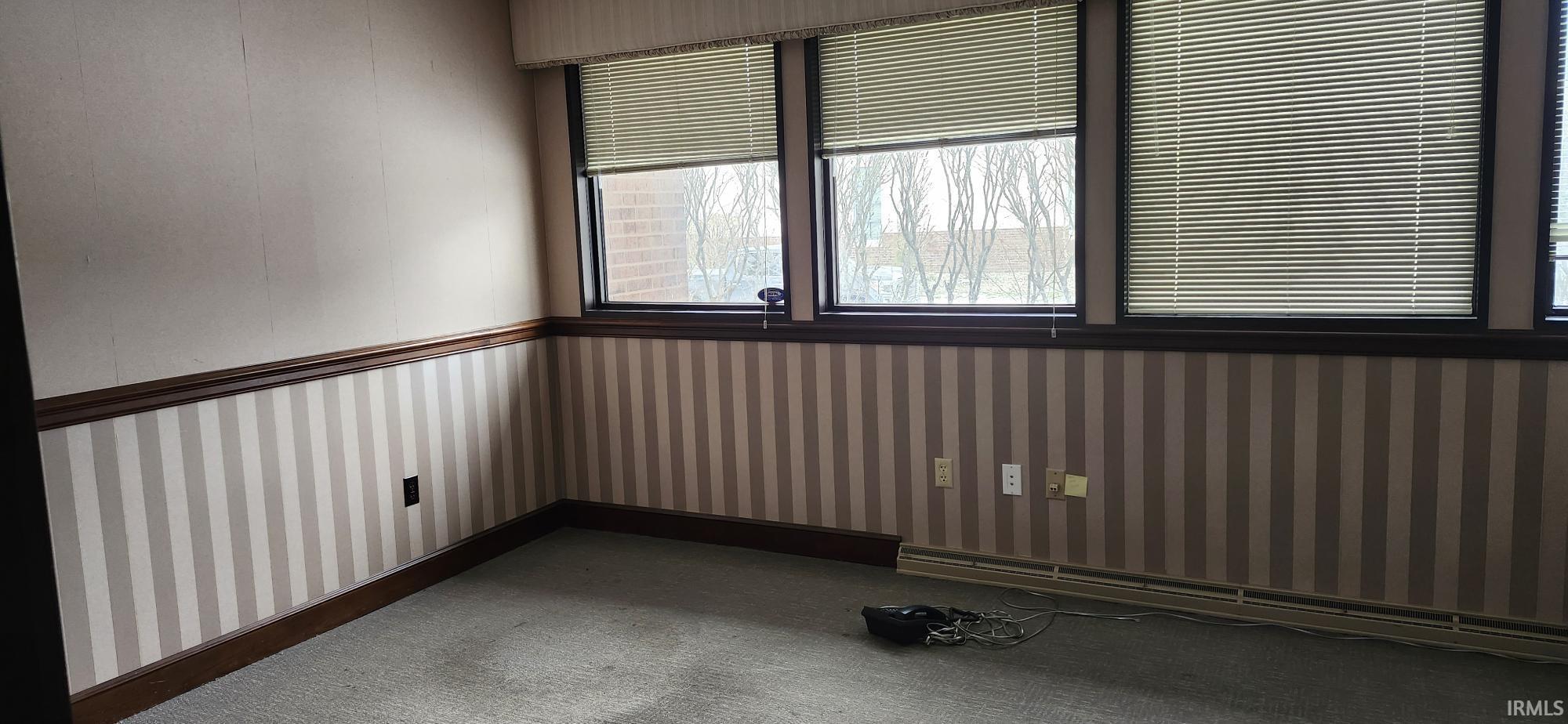 Spare room featuring baseboard heating, wallpapered walls, and dark carpet