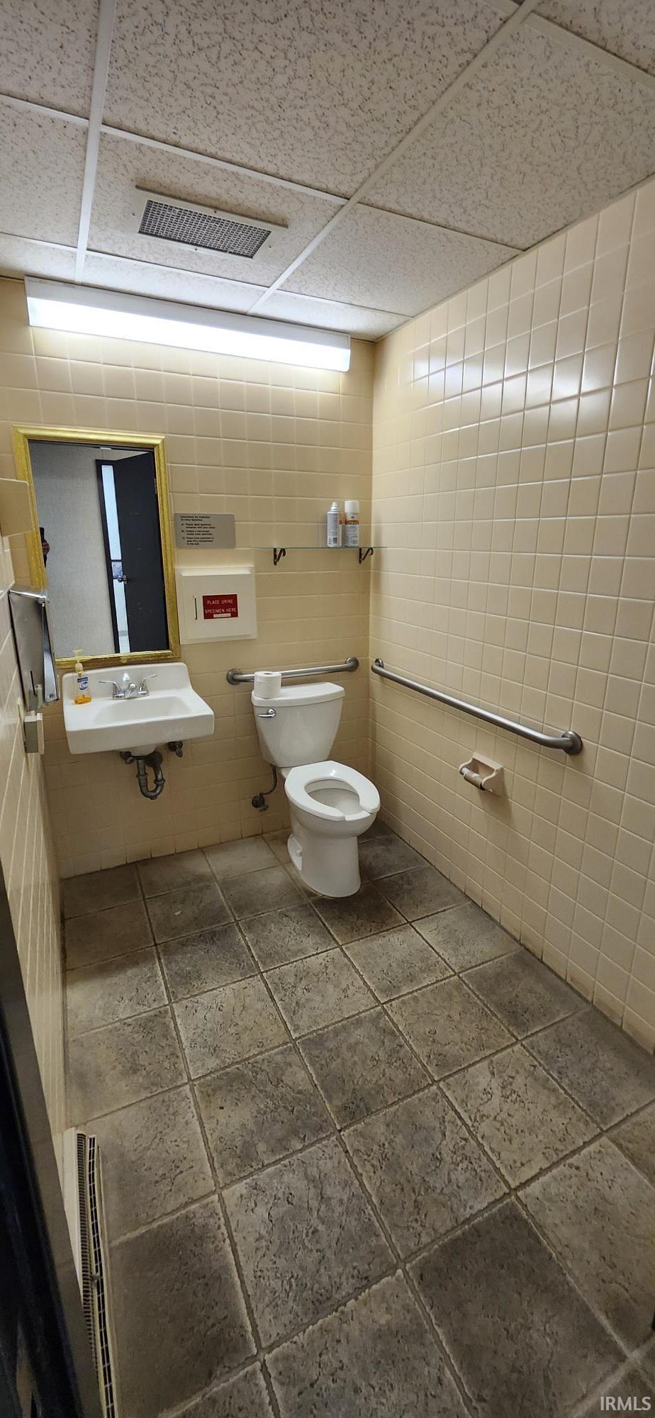 Bathroom with a drop ceiling, stone tile flooring, and tile walls