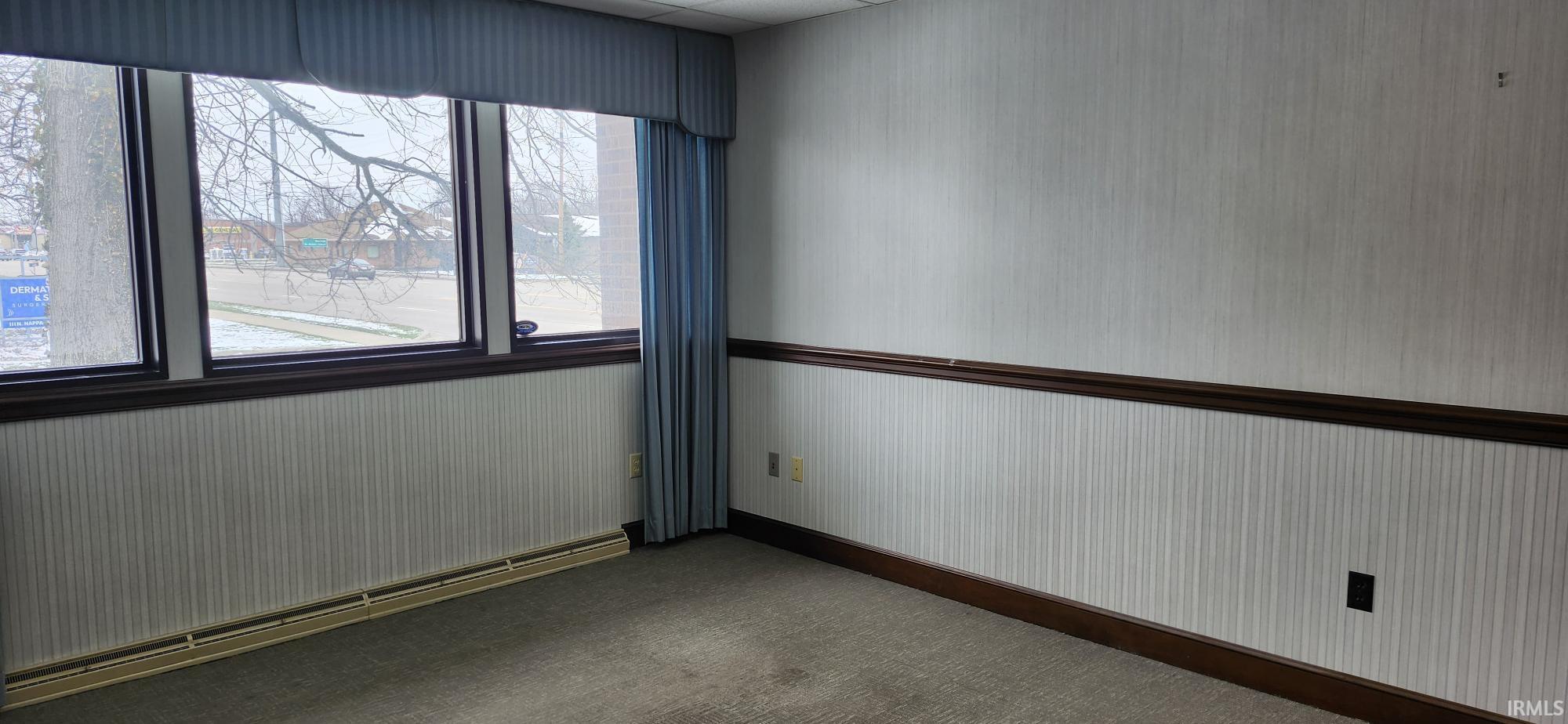 Unfurnished room featuring baseboard heating and dark carpet