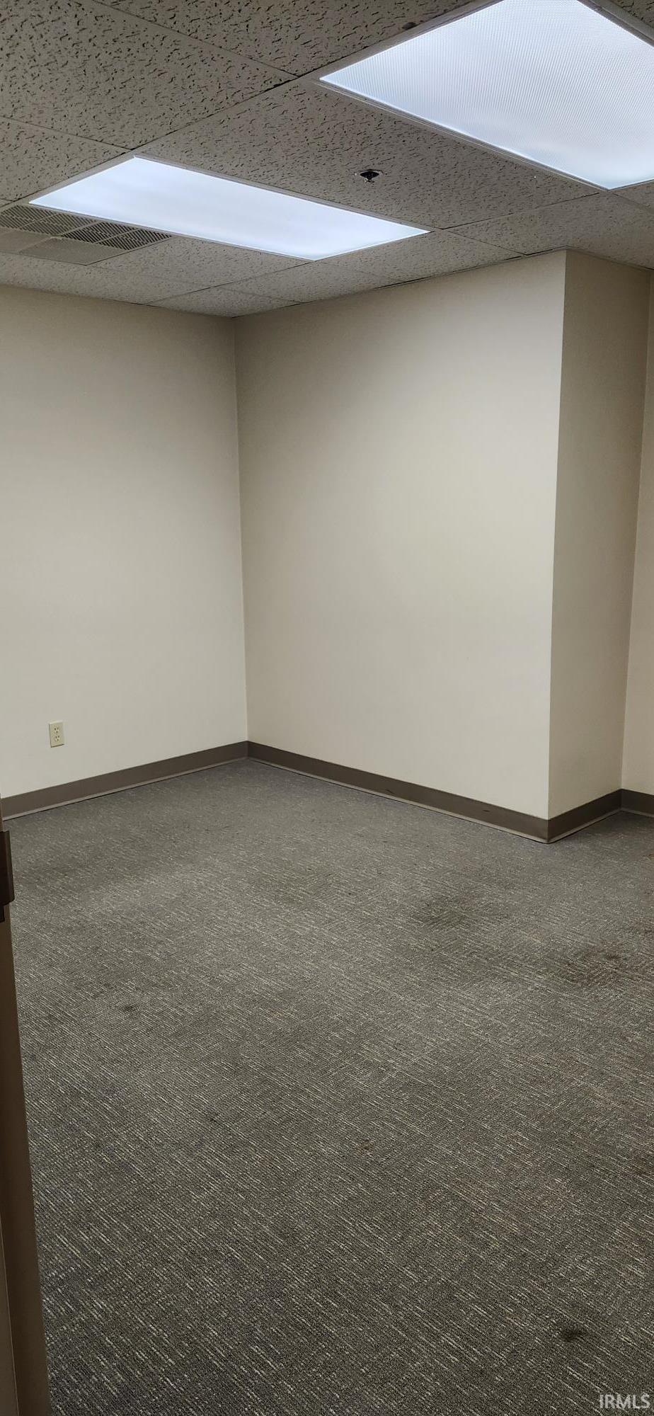 Spare room featuring dark colored carpet and a drop ceiling