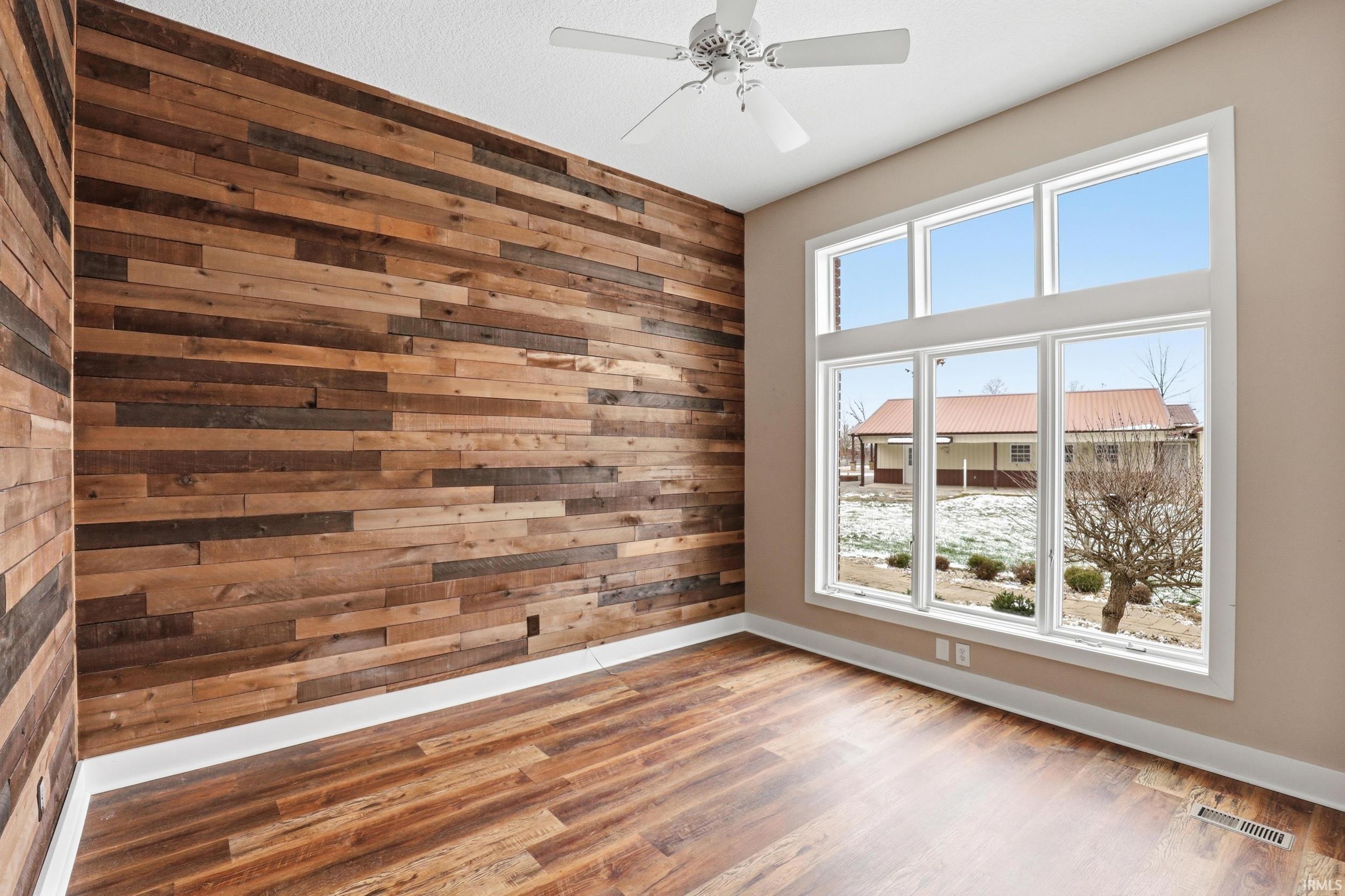 Empty room with wood walls, a ceiling fan, and wood finished floors