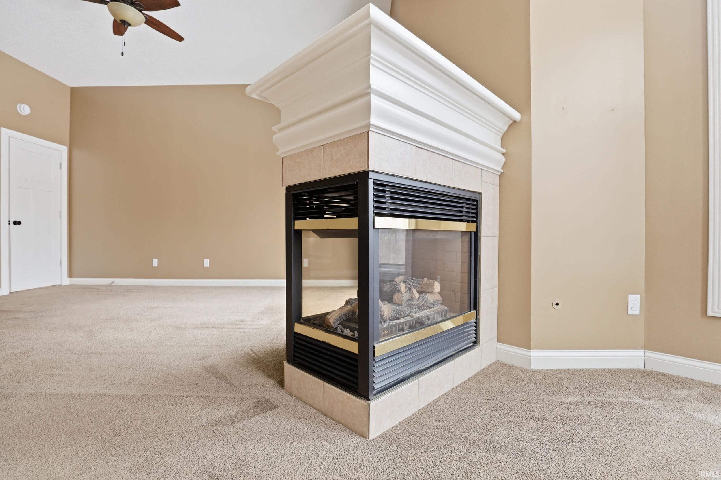 Detailed view of a tile fireplace, carpet flooring, and a ceiling fan