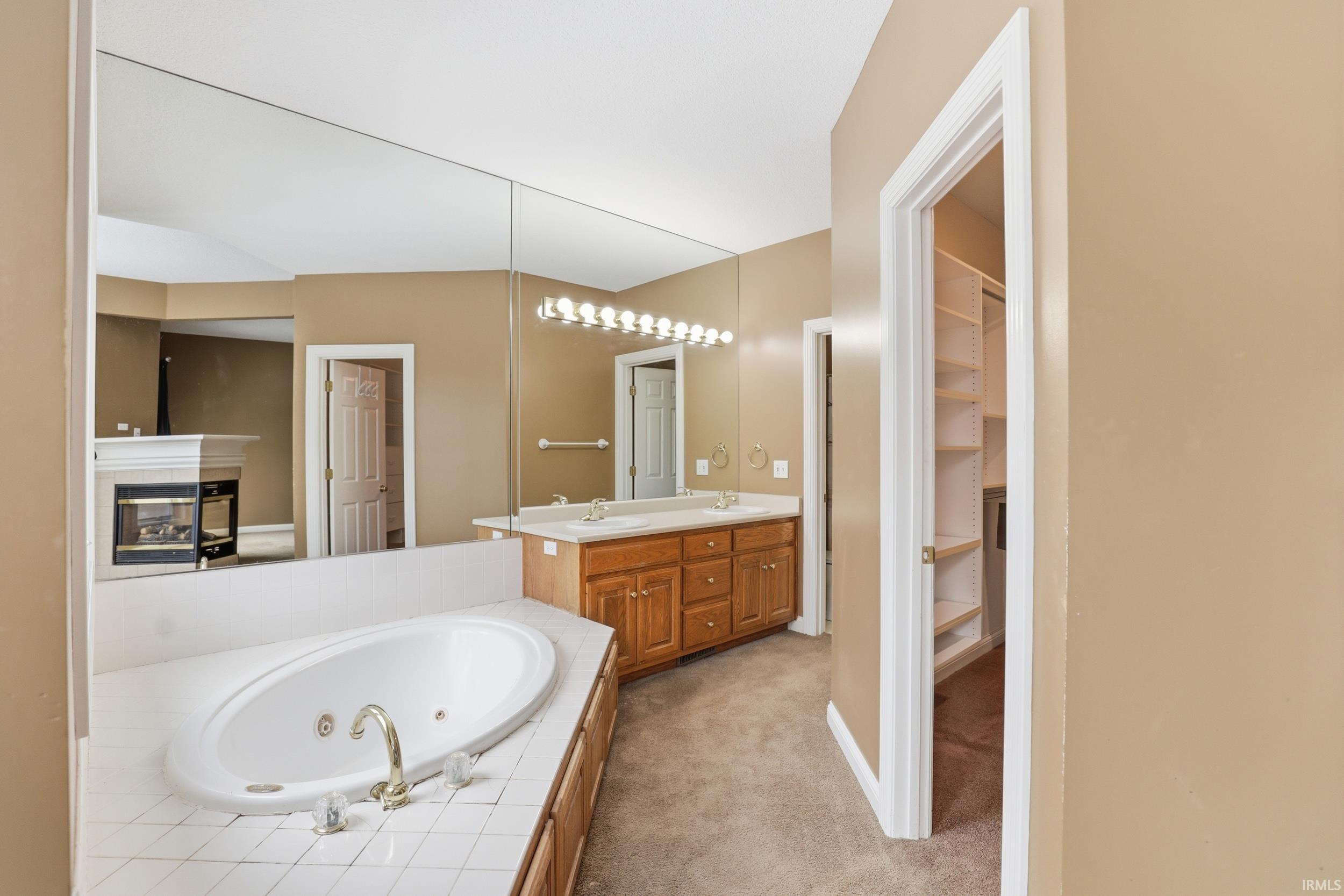 Full bathroom featuring double vanity, light carpet, a tub with jets, a spacious closet, and a tile fireplace