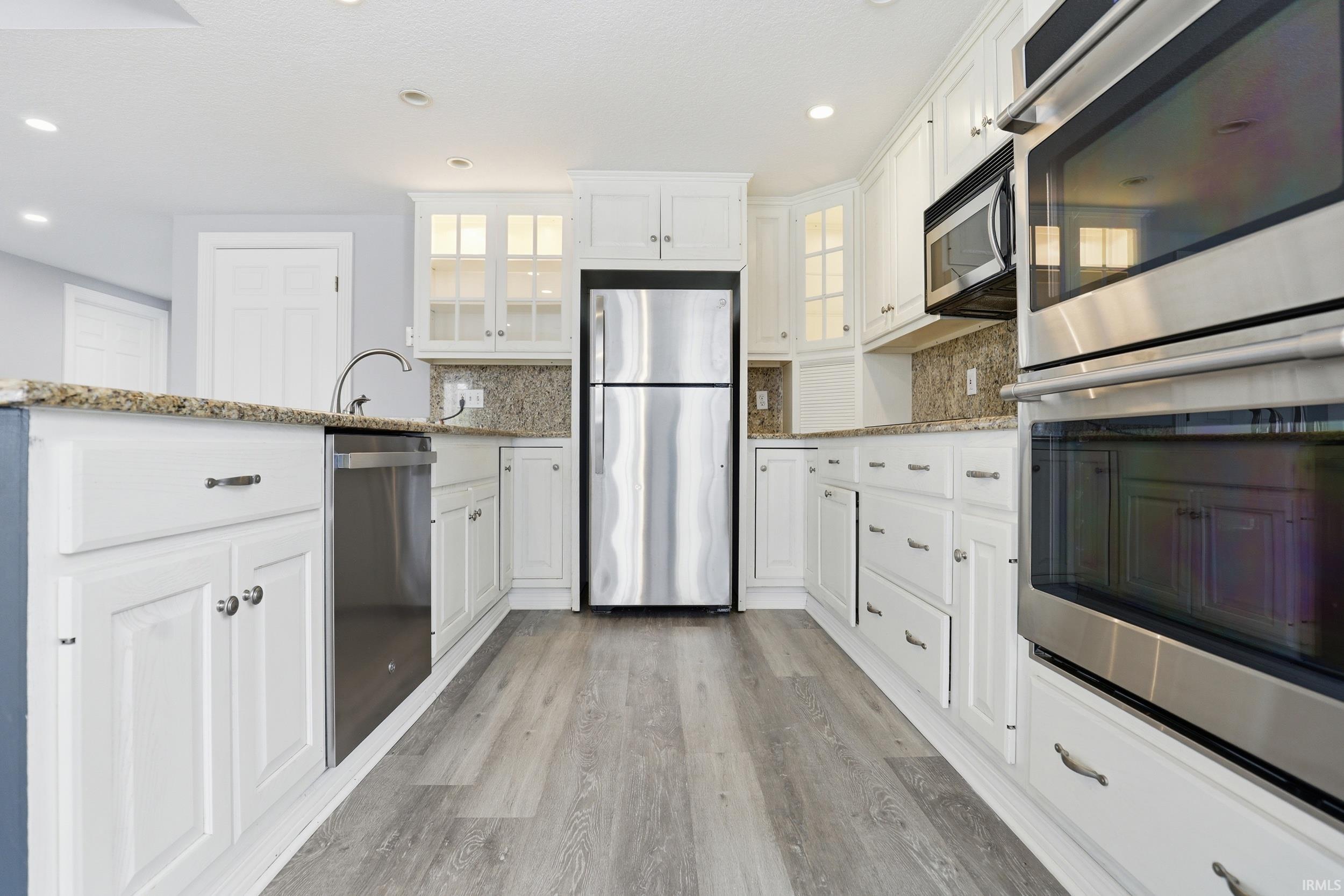 Kitchen featuring glass fronted cabinets, stainless steel appliances, light stone counters, white cabinets, and recessed lighting