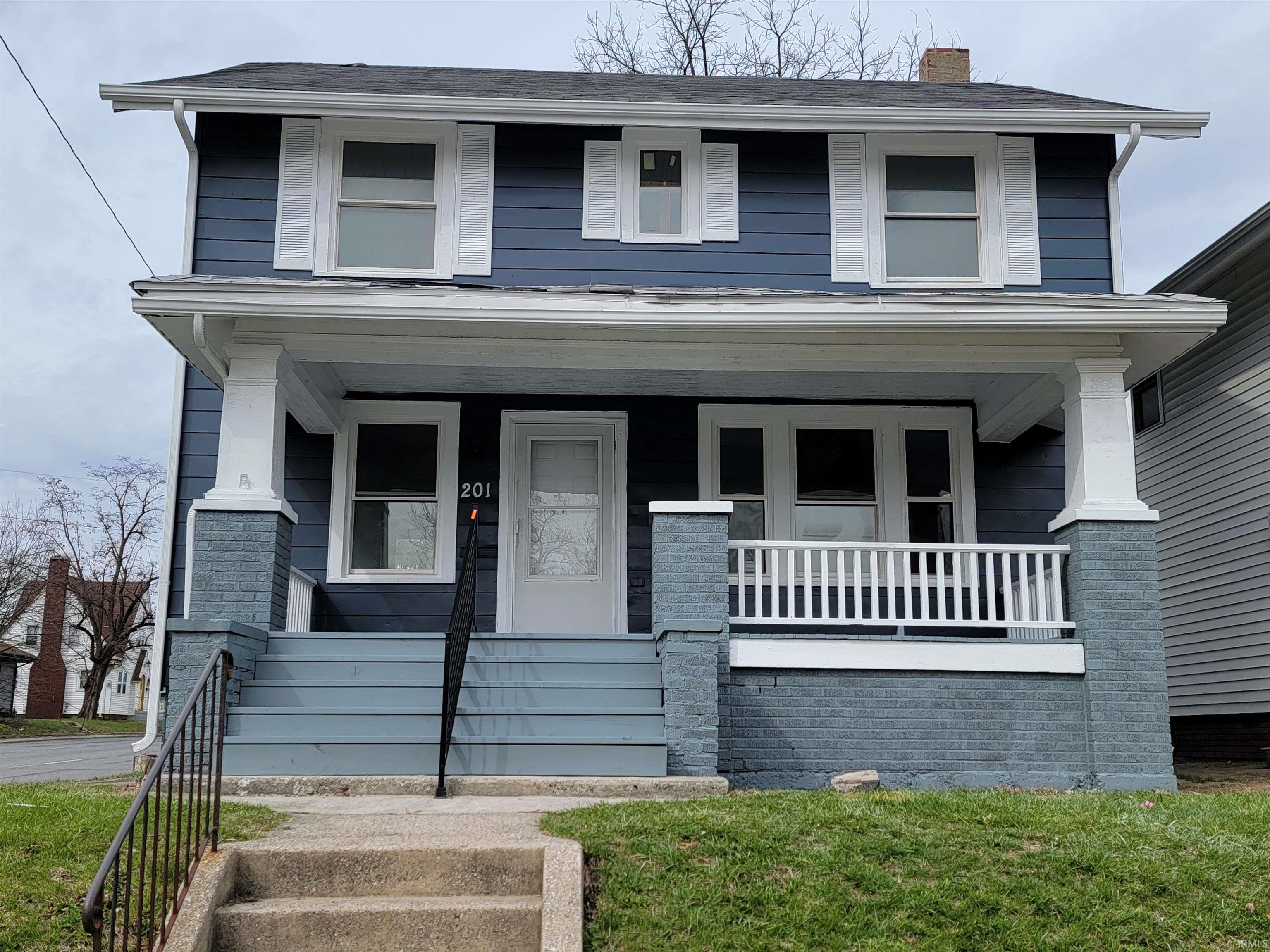 American foursquare style home featuring covered porch, a chimney, and a front yard