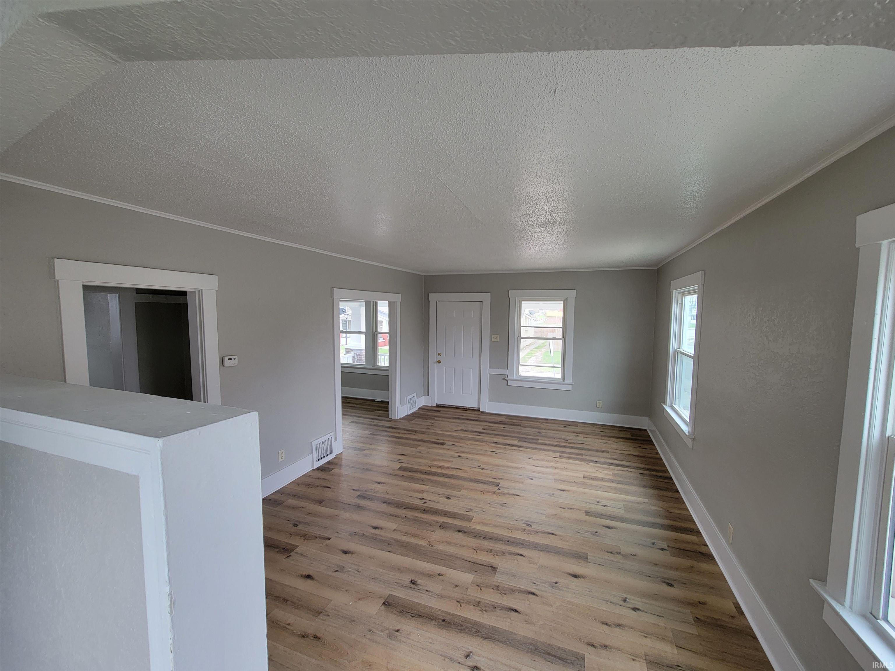 Unfurnished living room featuring a textured ceiling, light wood-style floors, and ornamental molding