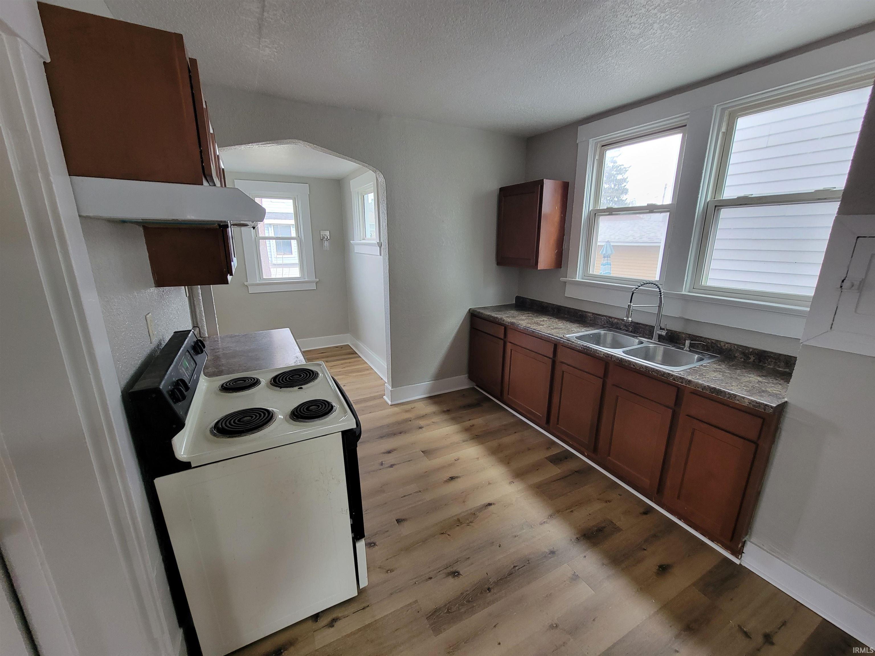 Kitchen featuring white electric stove, dark countertops, light wood-type flooring, a textured ceiling, and arched walkways