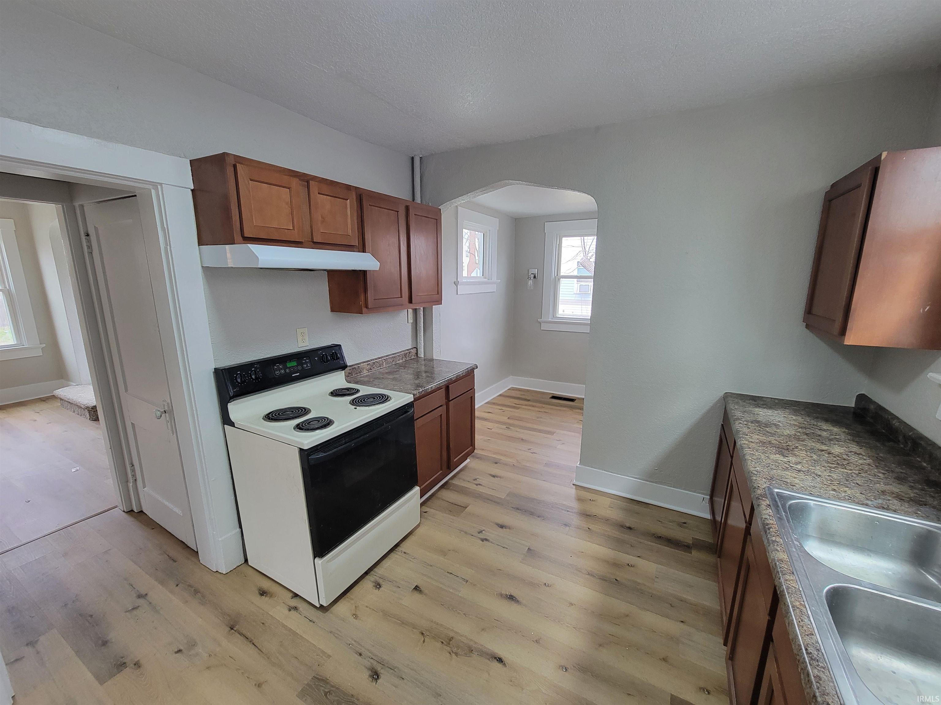 Kitchen with range with electric cooktop, light wood finished floors, arched walkways, wood finish cabinetry, and a textured ceiling