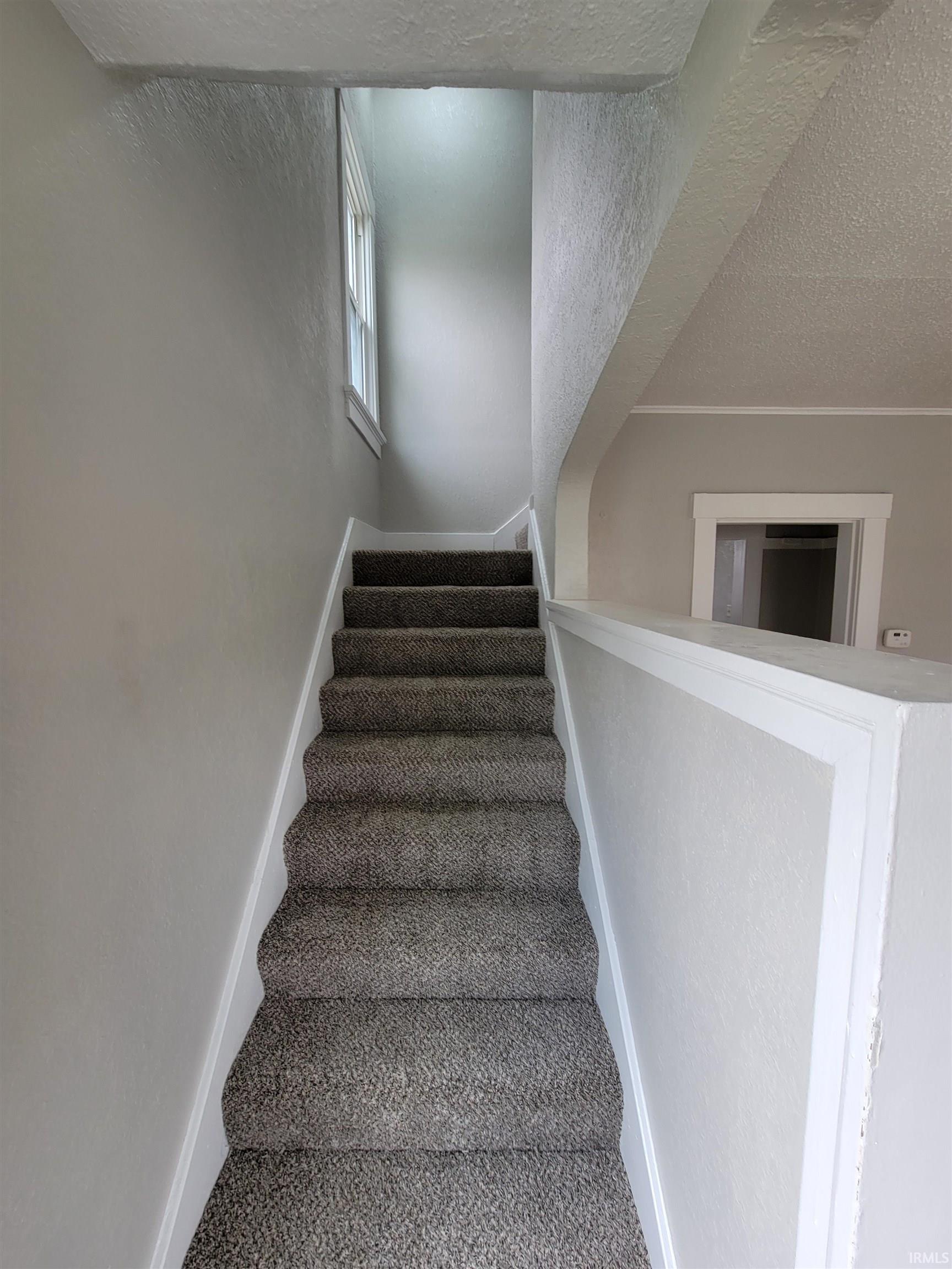 Staircase with a textured ceiling and a textured wall