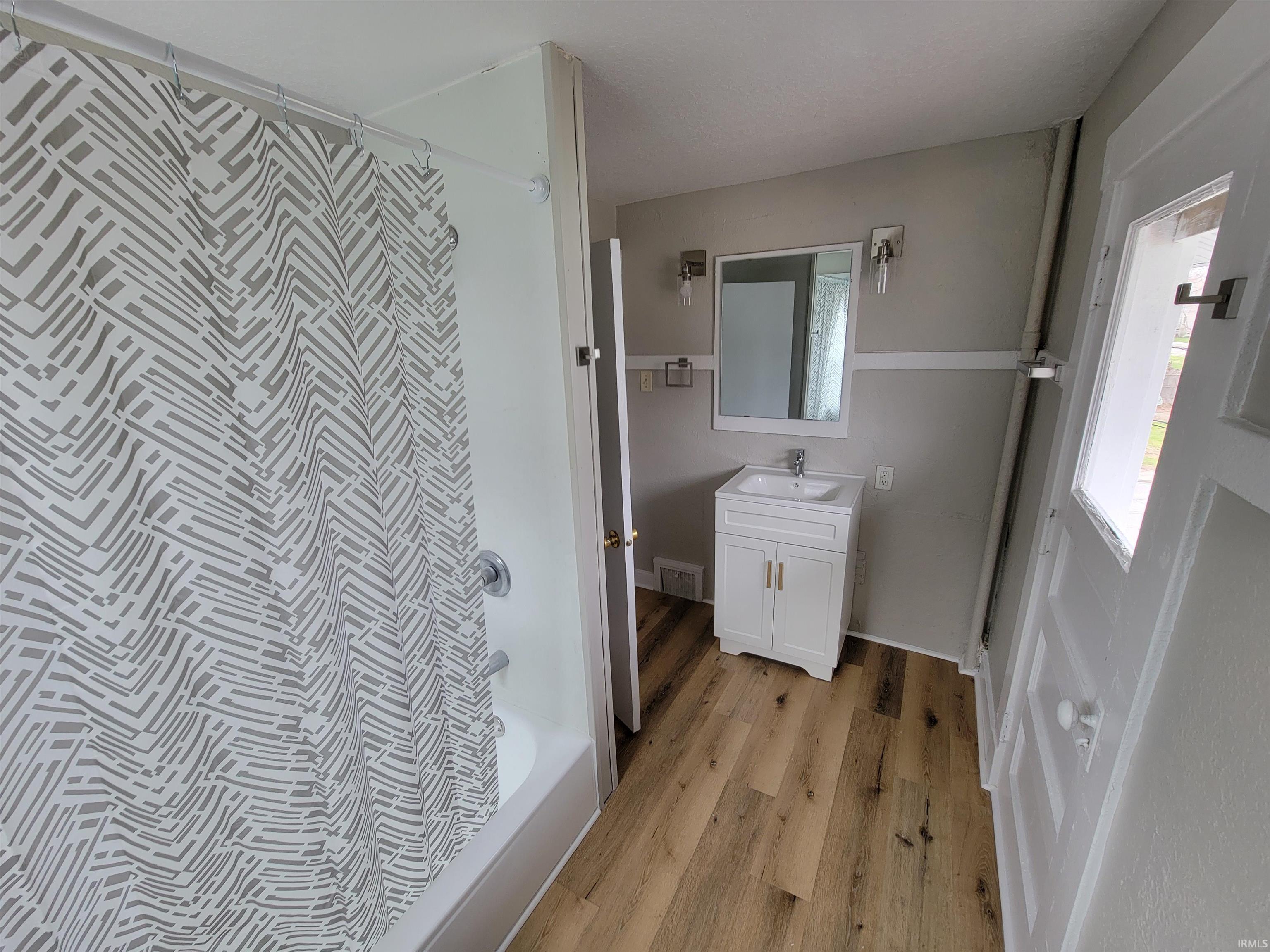 Bathroom with vanity, shower / bath combination with curtain, and light wood finished floors