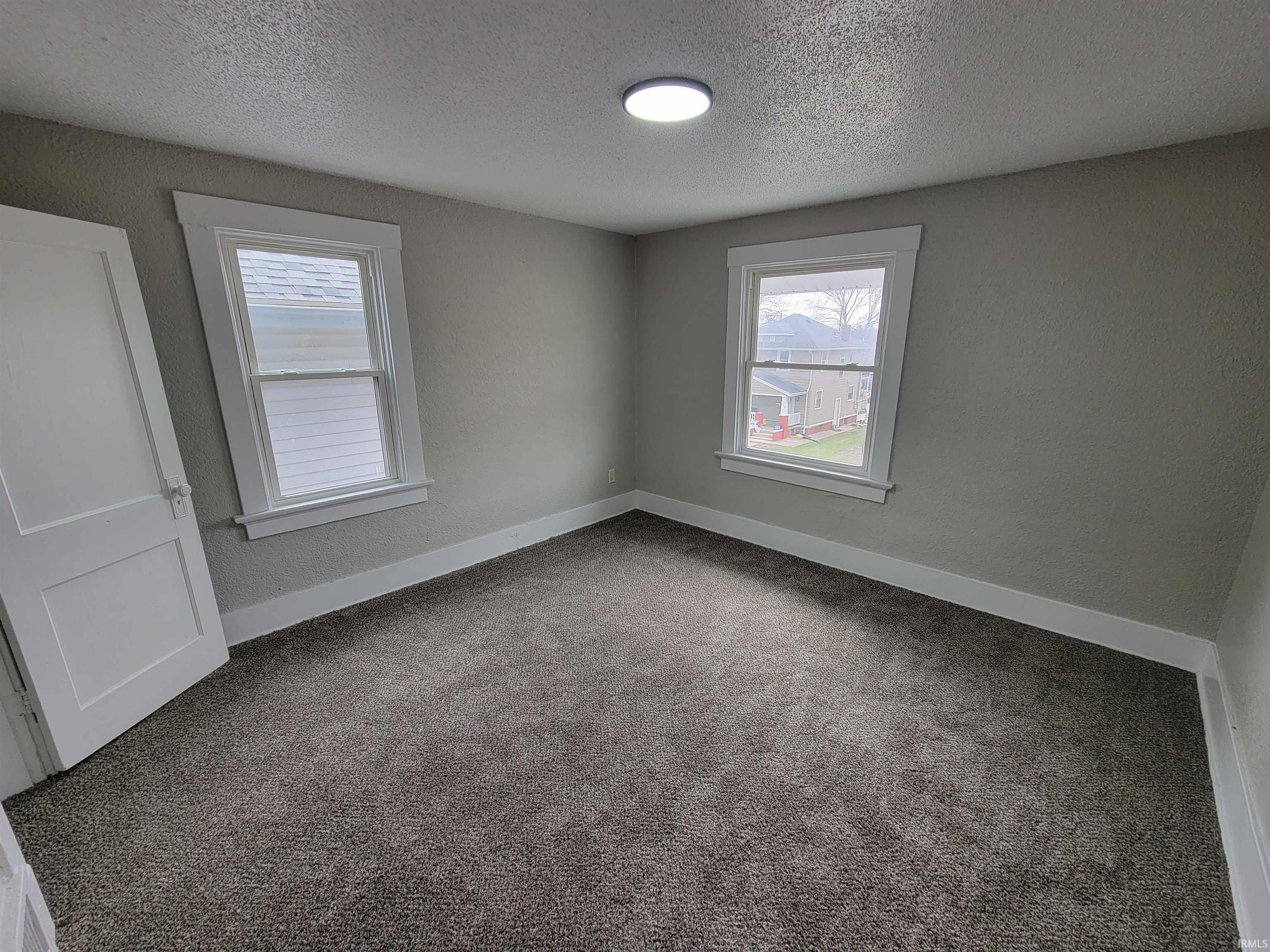 Carpeted spare room with a textured ceiling, plenty of natural light, and a textured wall