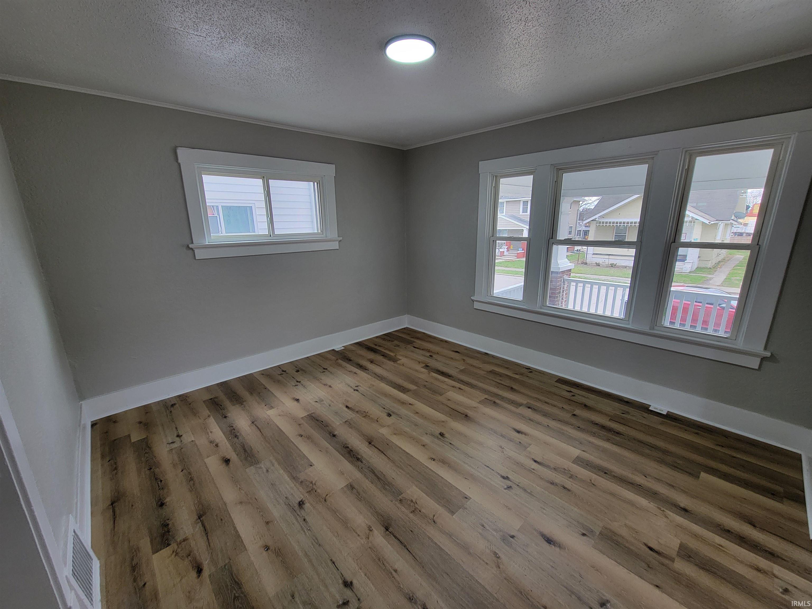 Unfurnished room featuring light wood-style floors, a textured ceiling, and crown molding