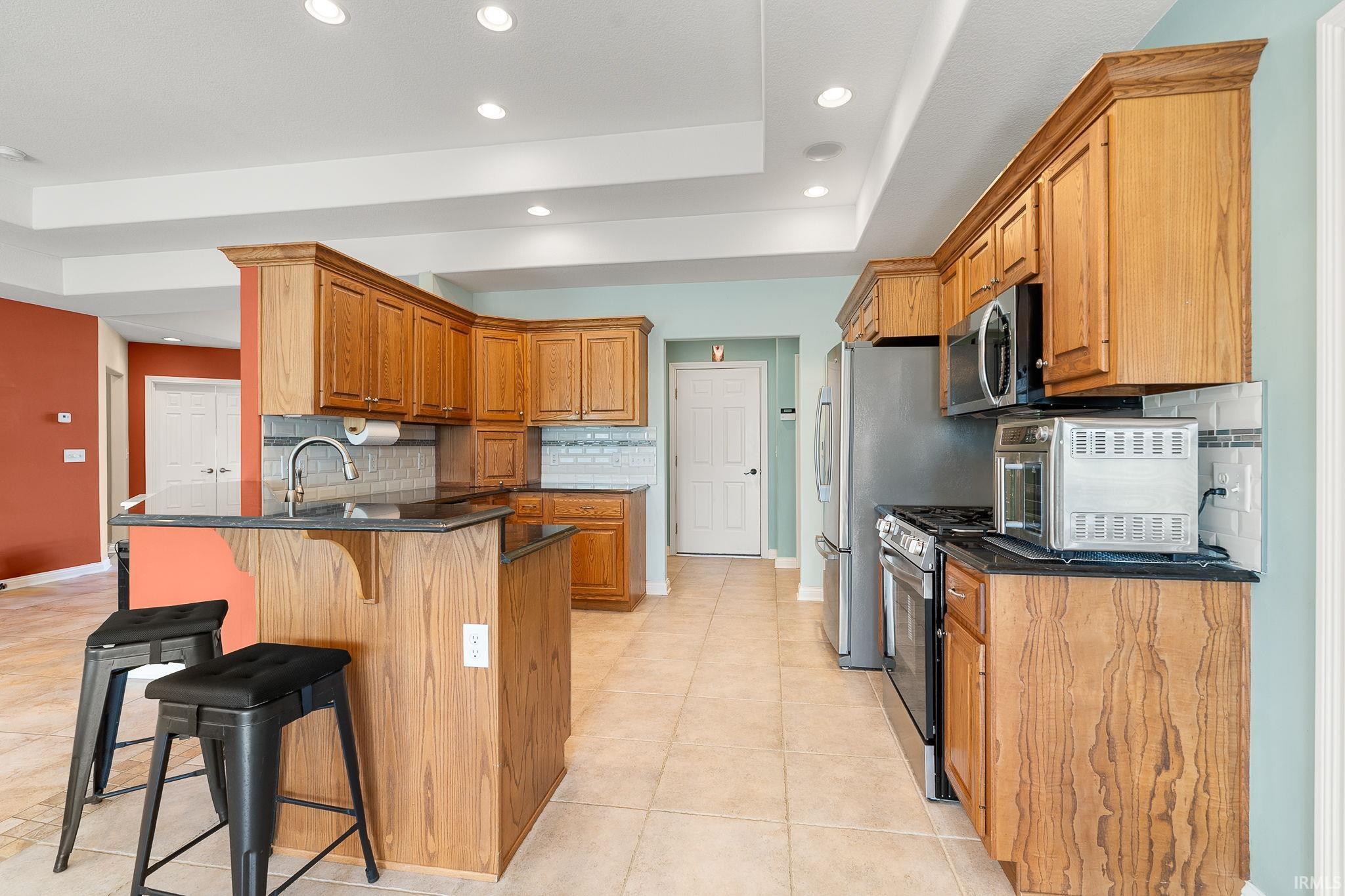 Kitchen featuring a peninsula, a breakfast bar, backsplash, wood finish cabinets, and a raised ceiling