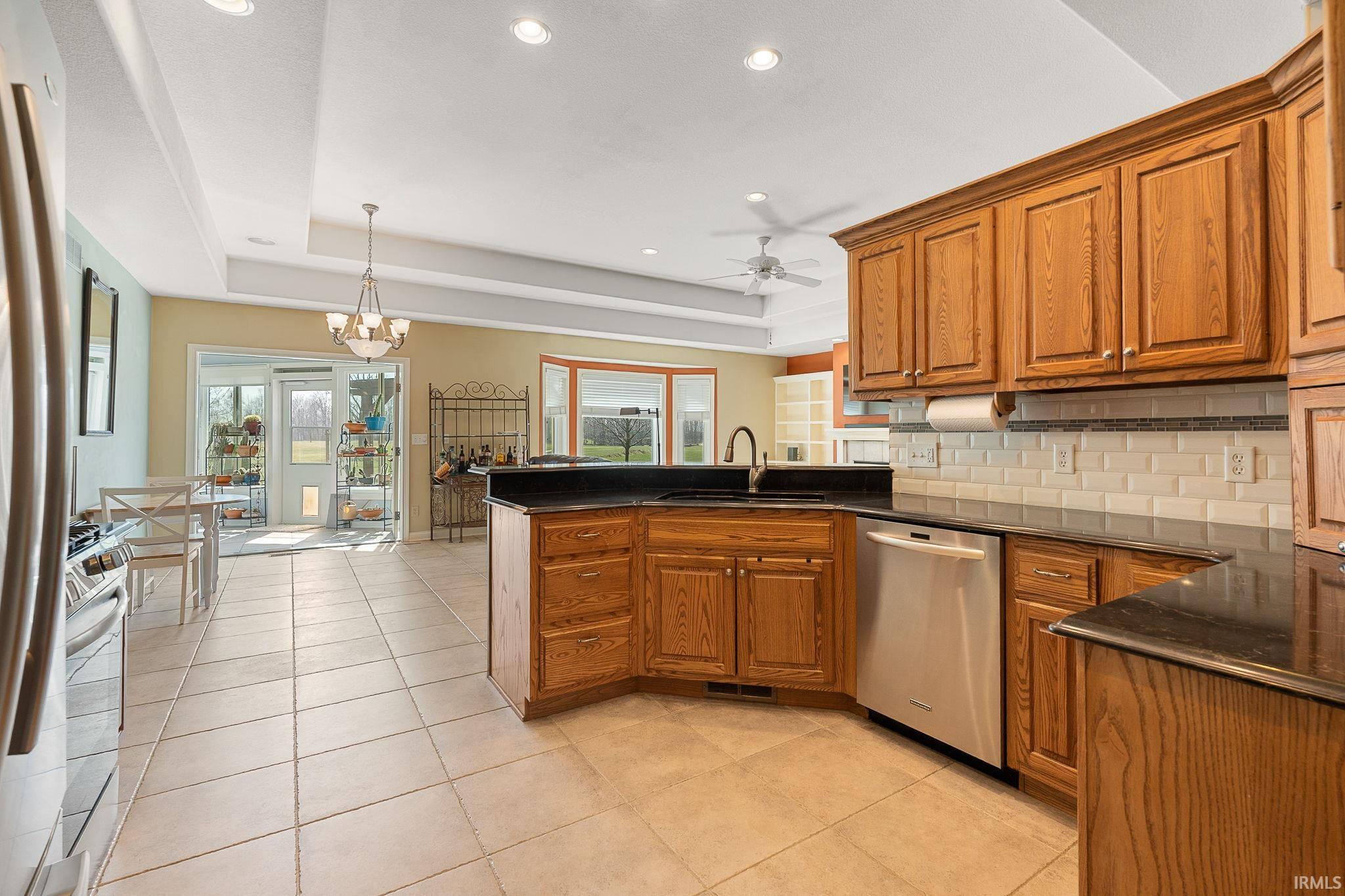 Kitchen with wood finish cabinetry, a peninsula, ceiling fan, stainless steel appliances, and light tile patterned flooring