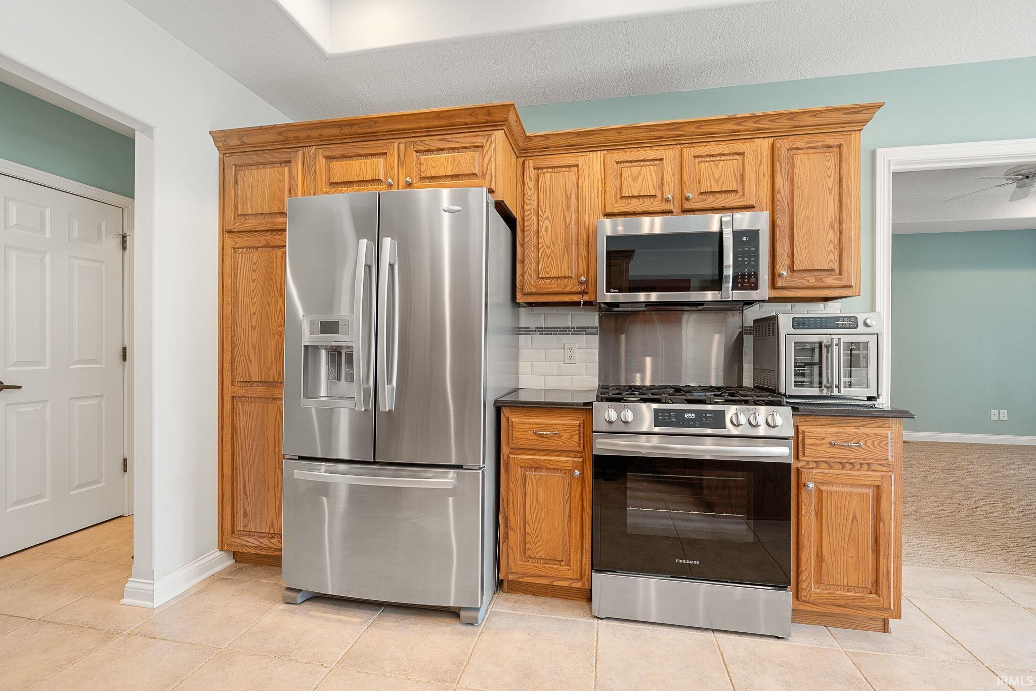 Kitchen with stainless steel appliances, light tile patterned floors, ceiling fan, and wood finish cabinets