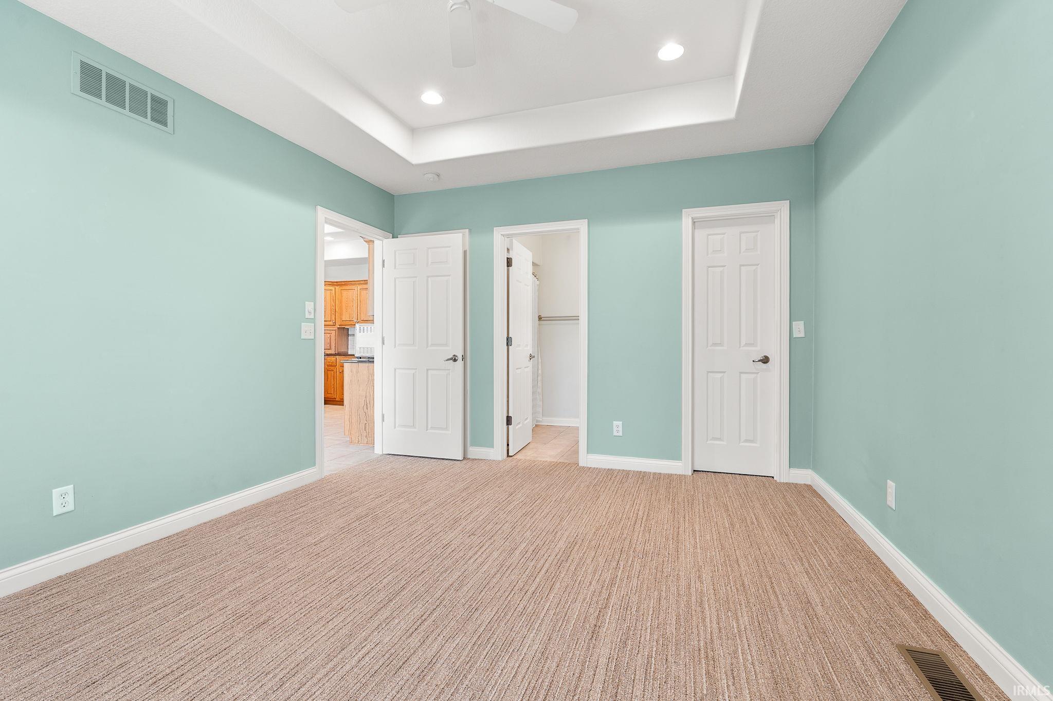Unfurnished bedroom featuring a walk in closet, light colored carpet, ceiling fan, a raised ceiling, and recessed lighting