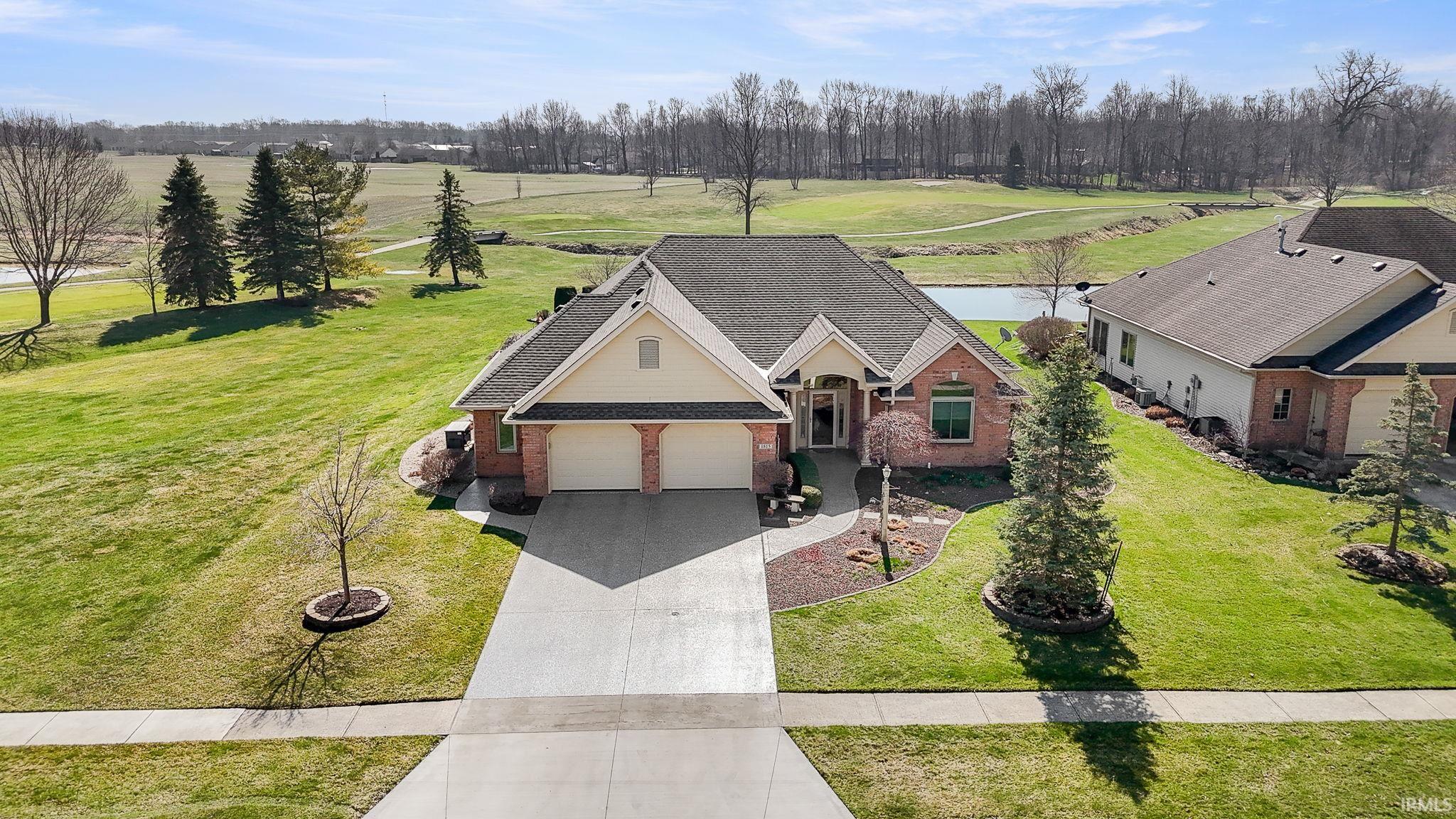 View of front facade with brick siding, a front lawn, driveway, a water view, and a shingled roof