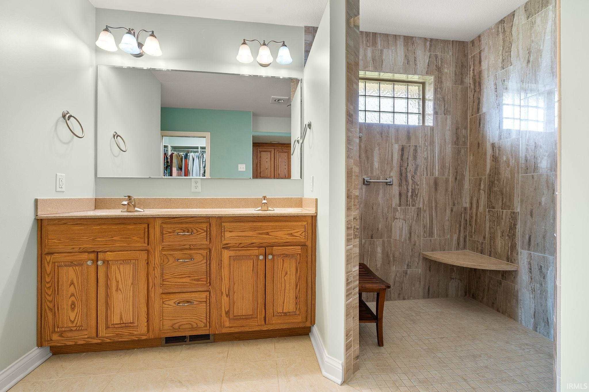 Bathroom featuring double vanity, a walk in shower, light tile patterned flooring, and a spacious closet