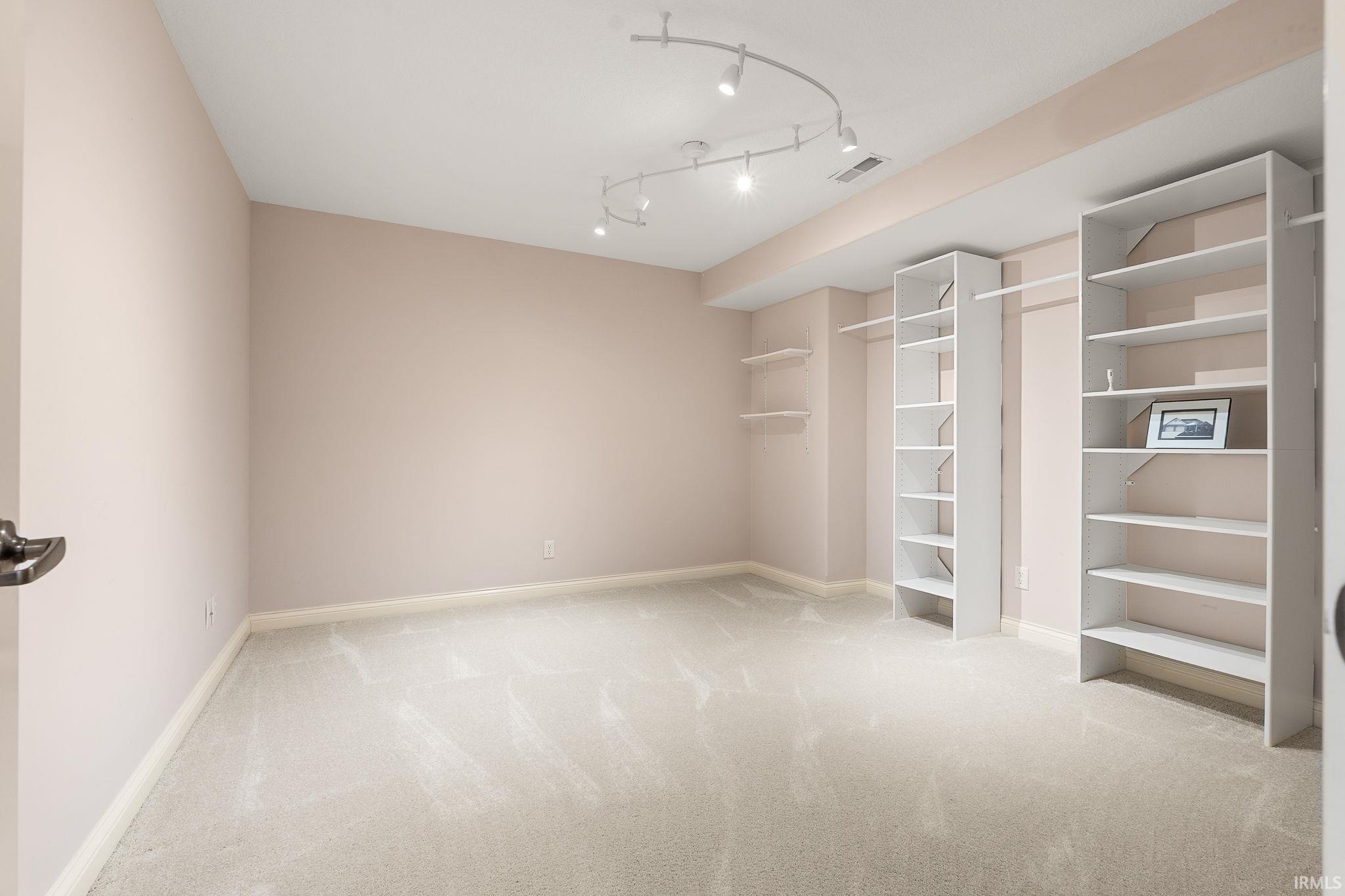 Unfurnished bedroom featuring light carpet and track lighting