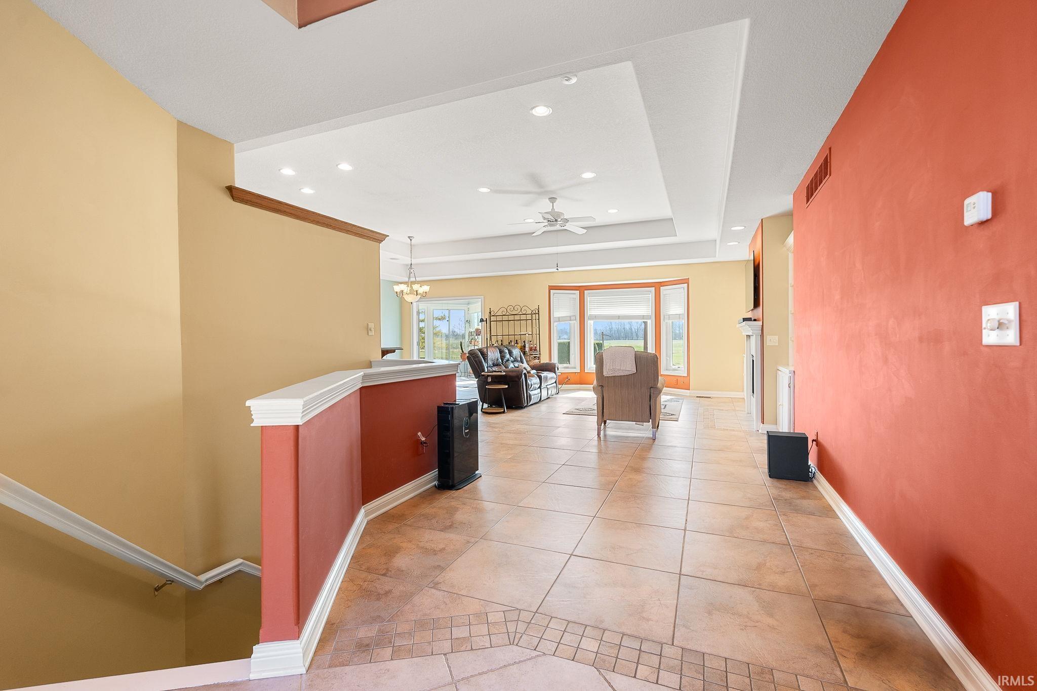 Corridor with recessed lighting, an upstairs landing, light tile patterned floors, and a raised ceiling