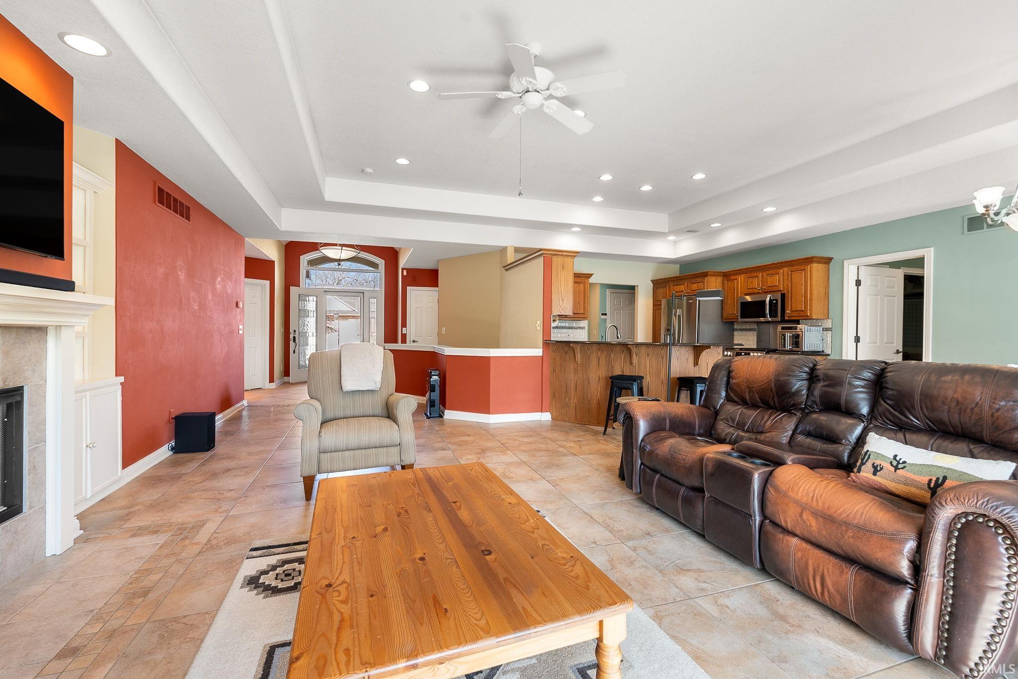 Living area with ceiling fan, a raised ceiling, a fireplace, light tile patterned floors, and suspended lighting