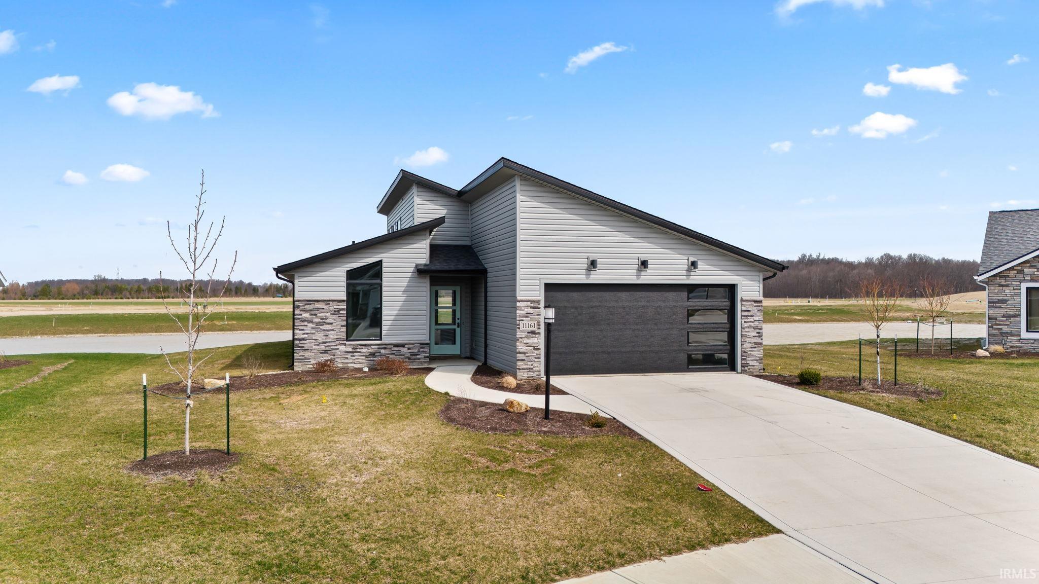 View of front of house featuring stone siding, concrete driveway, a front lawn, and a garage