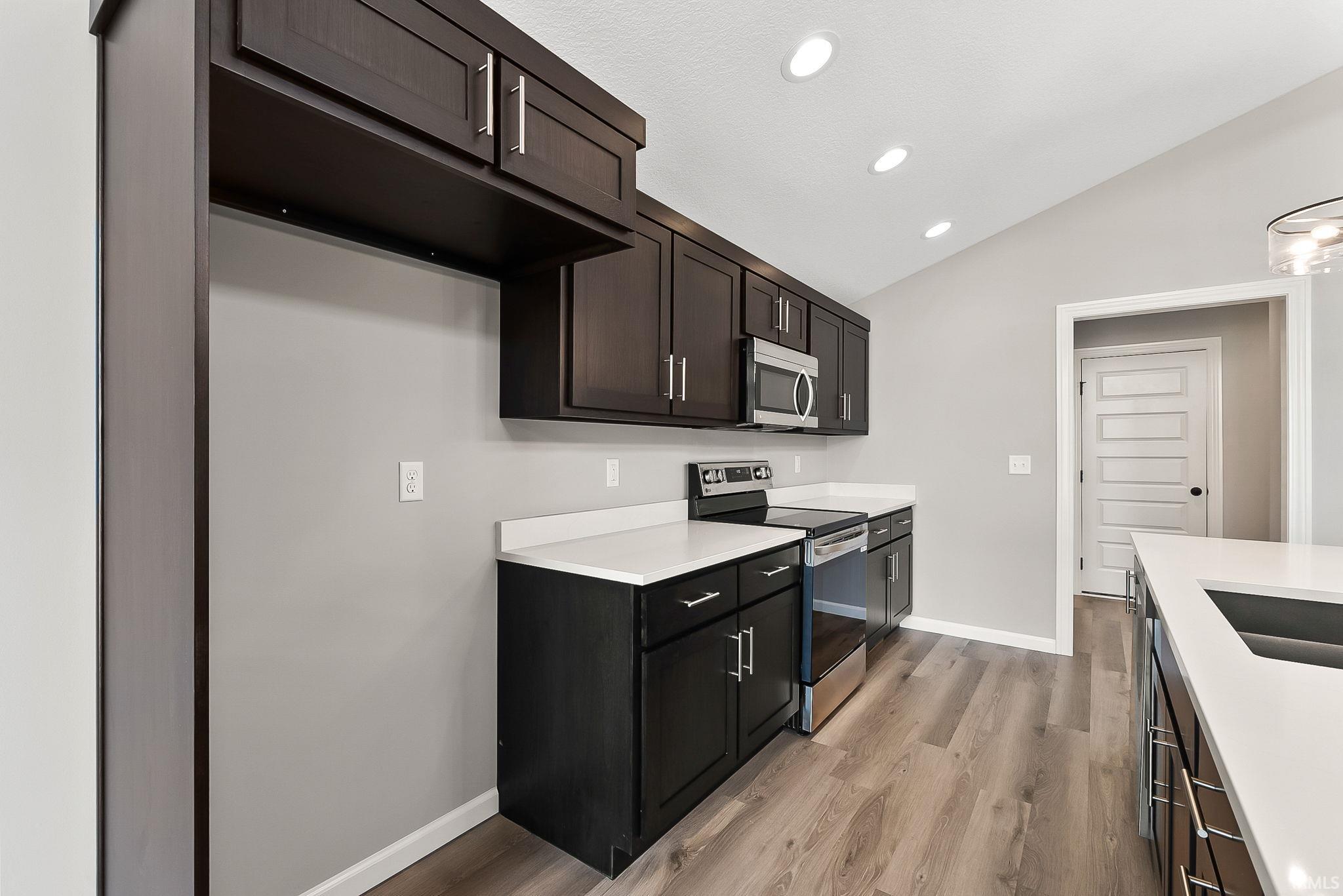 Kitchen featuring vaulted ceiling, stainless steel appliances, light wood-style flooring, recessed lighting, and dark wood finish cabinetry