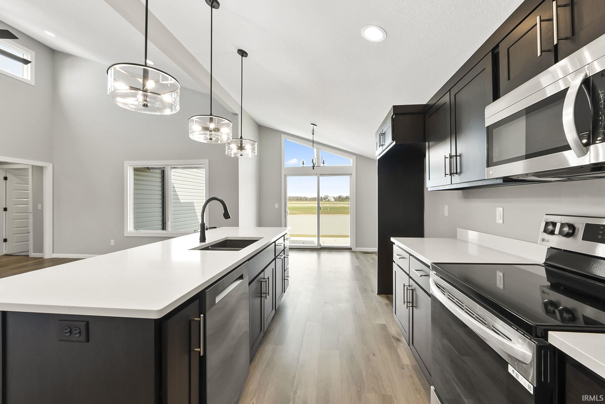 Kitchen with stainless steel appliances, light wood finished floors, a center island with sink, a chandelier, and vaulted ceiling