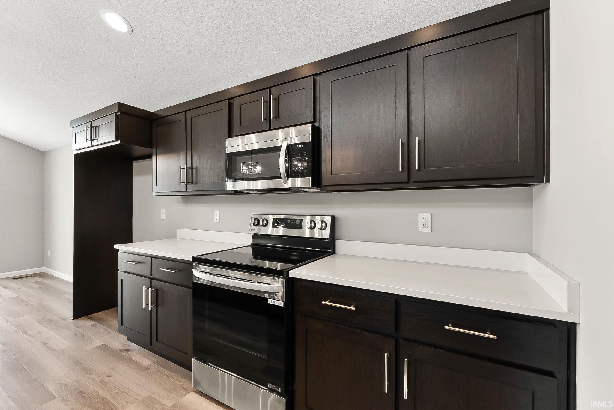 Kitchen with stainless steel appliances, light countertops, light wood-style flooring, and dark wood finish cabinets