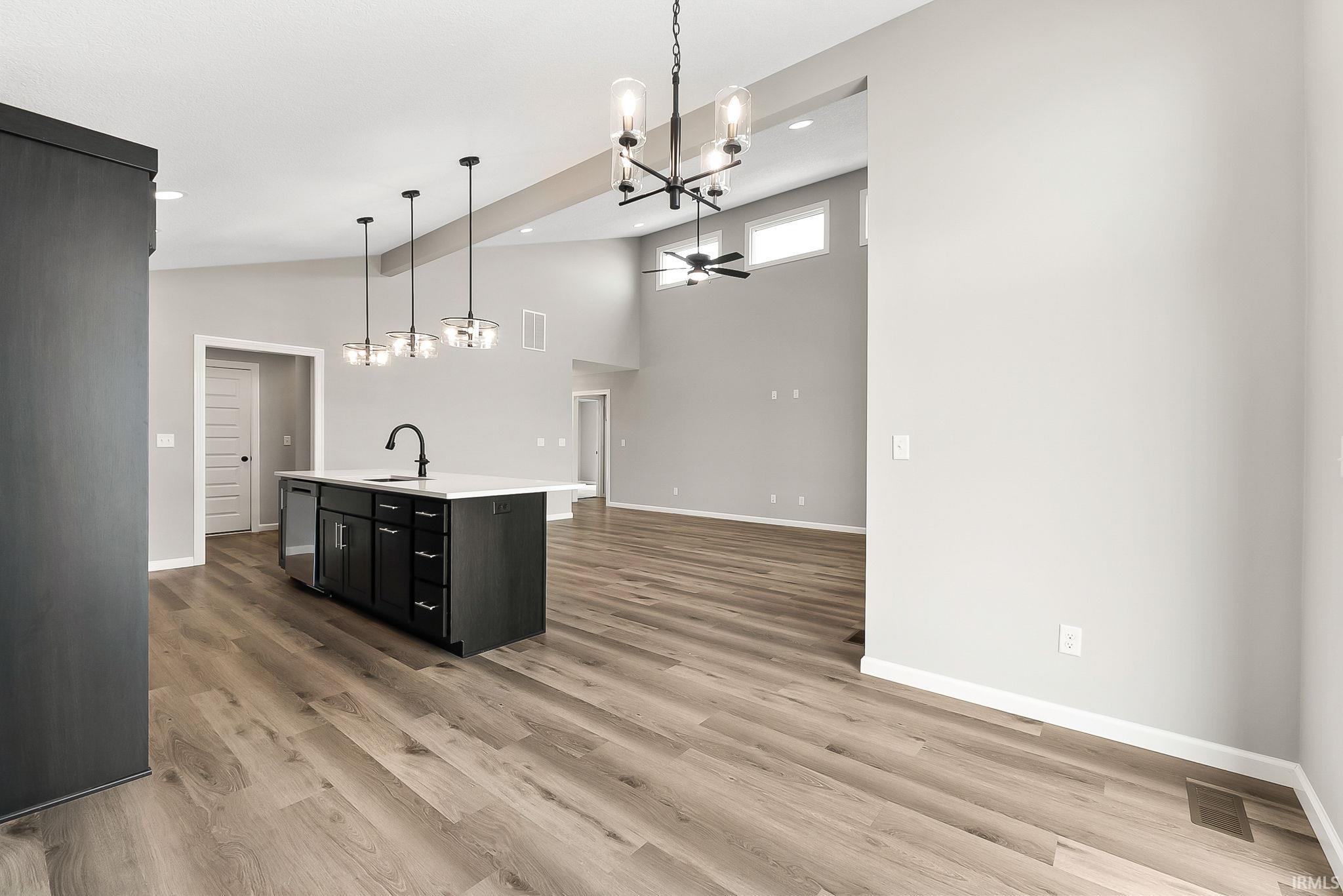 Kitchen featuring suspended lighting, open floor plan, a kitchen island with sink, light wood-type flooring, and a ceiling fan