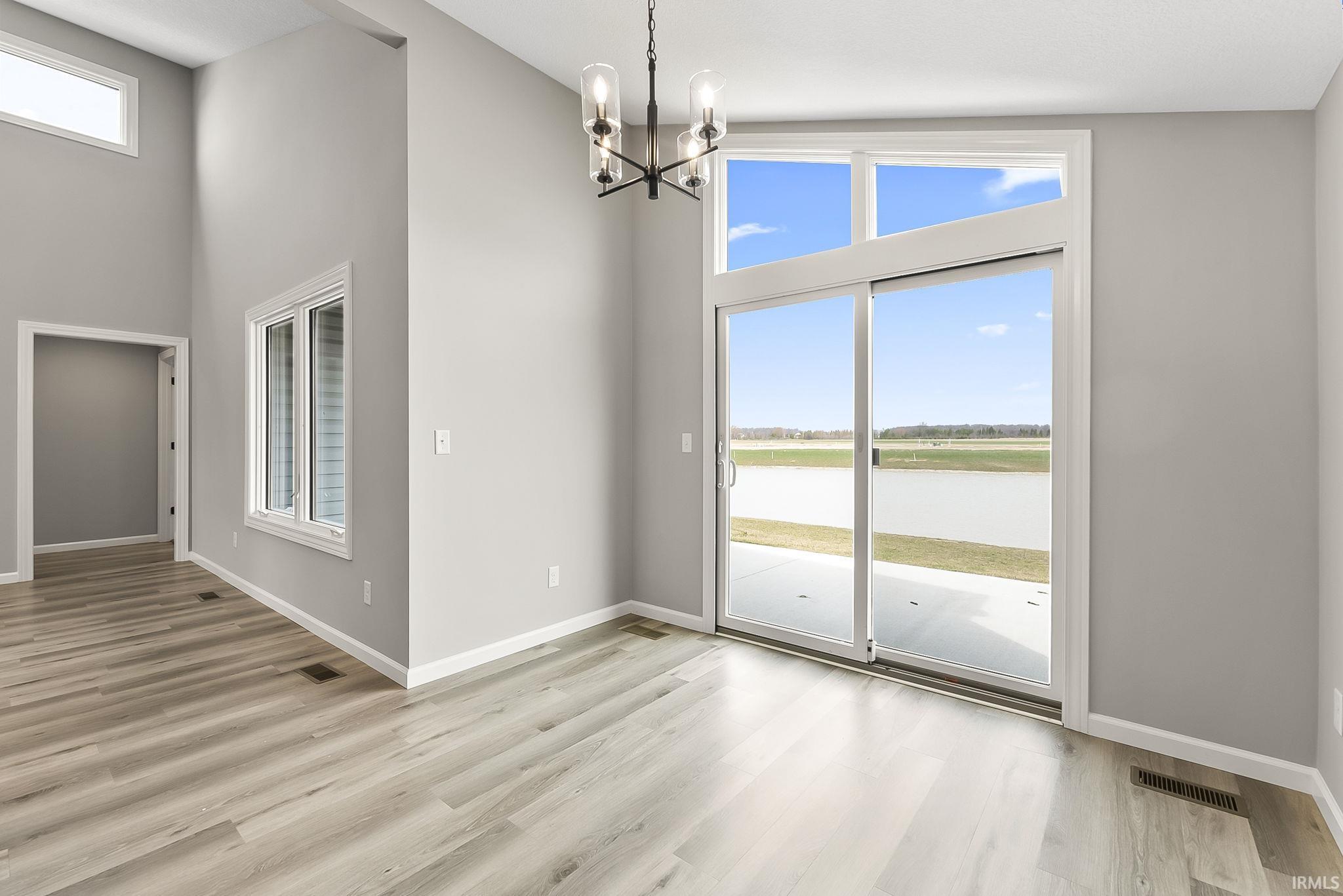 Unfurnished dining area with a water view, suspended lighting, a high ceiling, and light wood finished floors