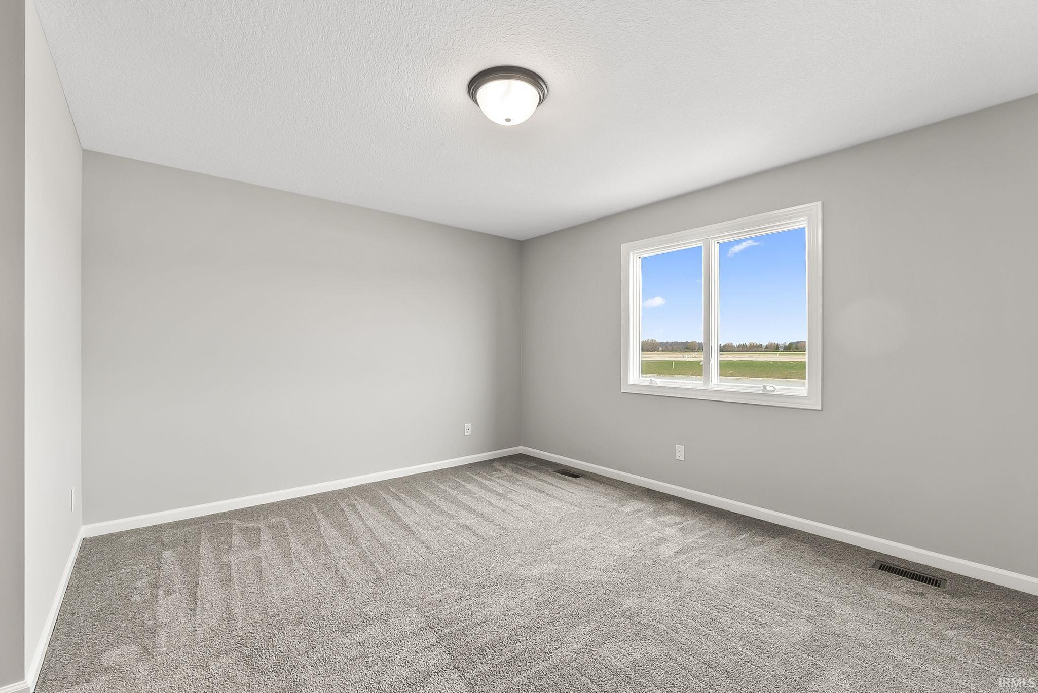 Empty room featuring light colored carpet and a textured ceiling