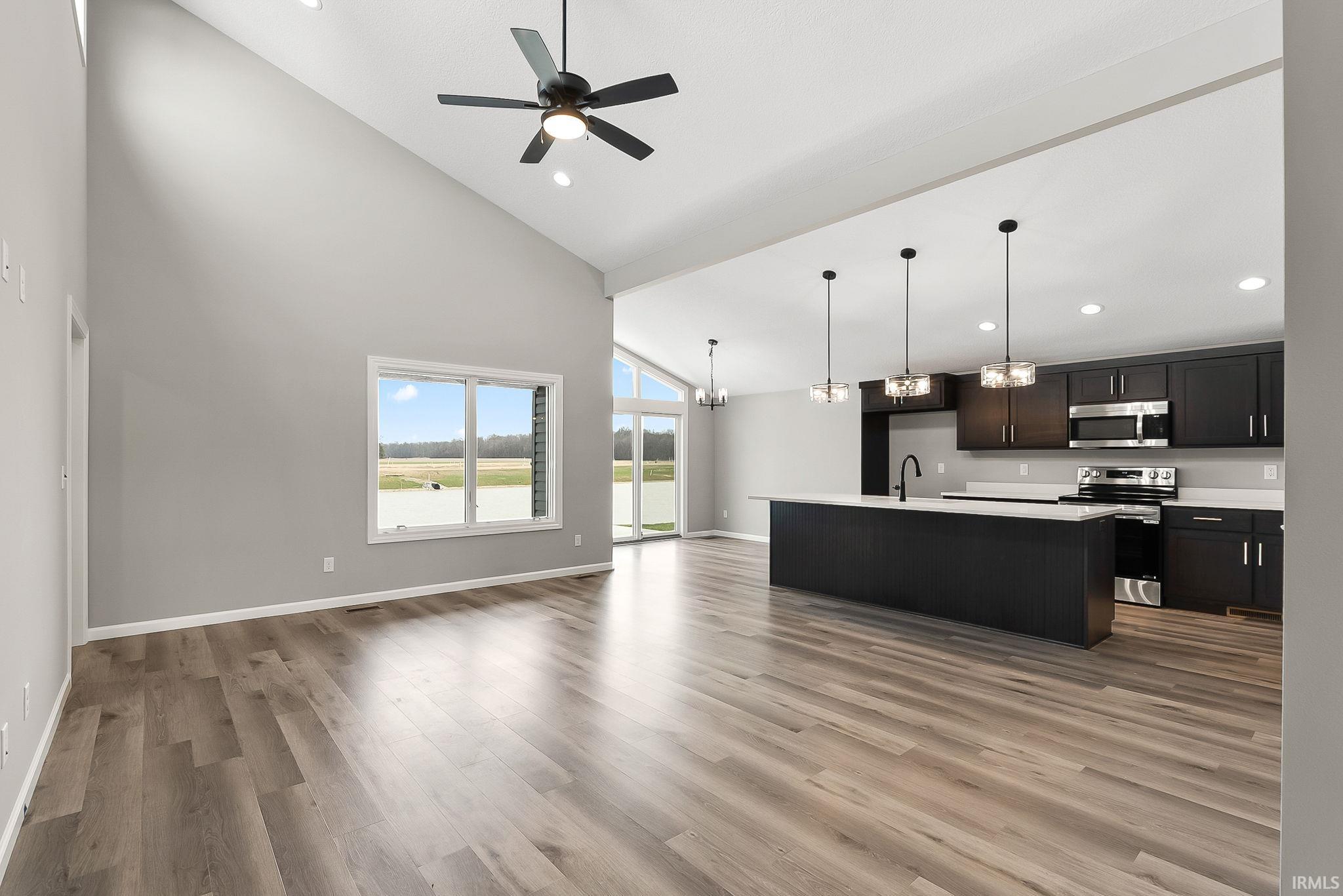 Kitchen featuring open floor plan, a kitchen island with sink, stainless steel appliances, a chandelier, and lofted ceiling