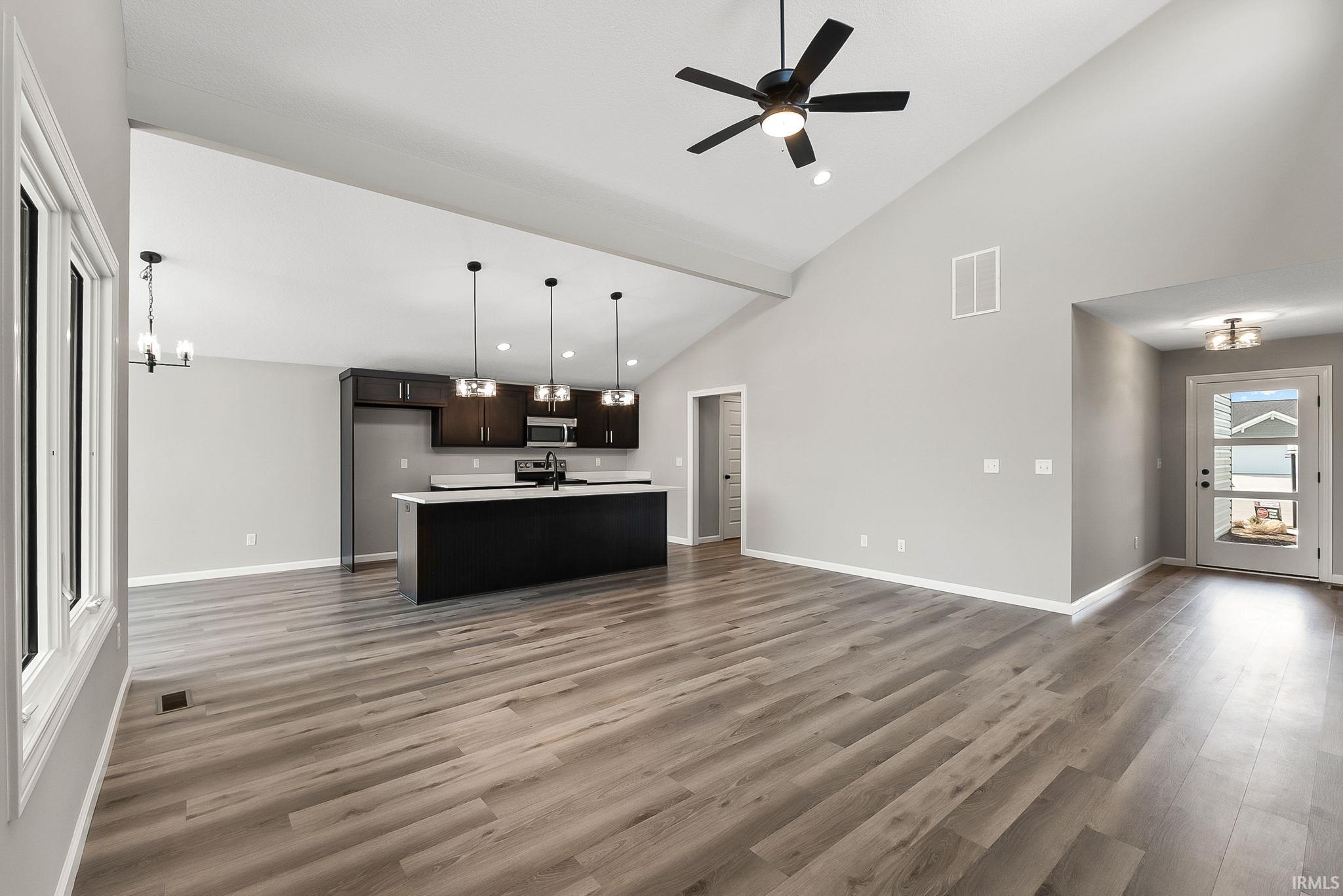 Kitchen with open floor plan, light countertops, an island with sink, a ceiling fan, and vaulted ceiling