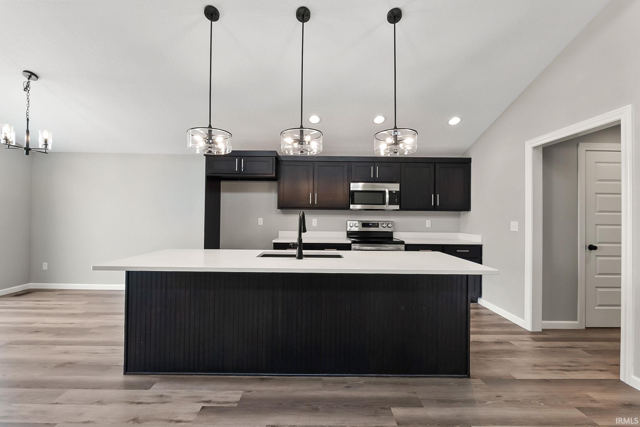 Kitchen featuring a chandelier, a center island with sink, stainless steel appliances, light wood finished floors, and lofted ceiling