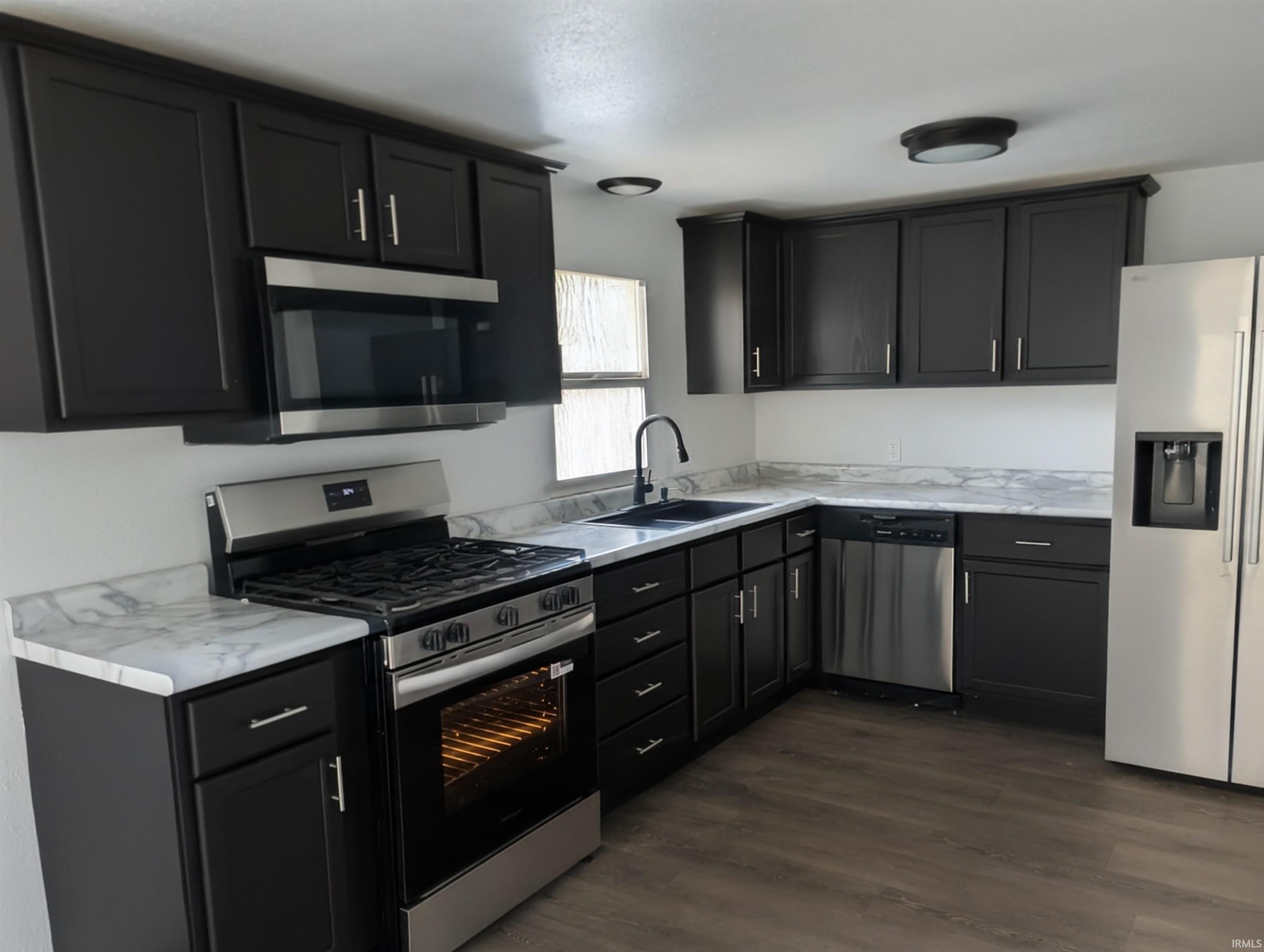 Kitchen with stainless steel appliances, light countertops, dark cabinets, and dark wood-style floors