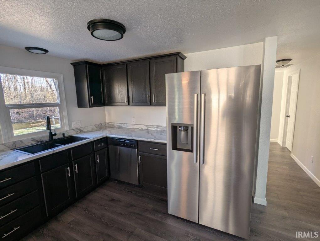 Kitchen with stainless steel appliances, dark wood-type flooring, a textured ceiling, light stone counters, and dark wood finish cabinetry