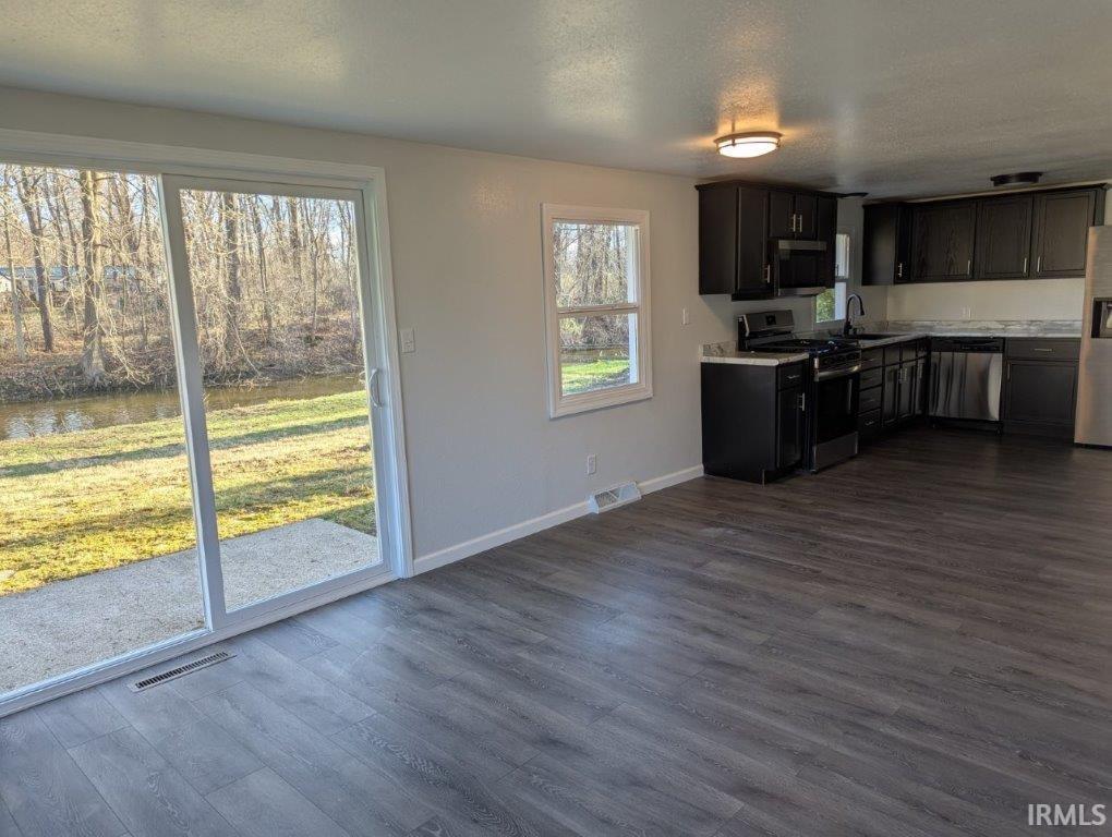 Kitchen featuring light countertops, stainless steel appliances, a textured ceiling, dark wood-style flooring, and a water view