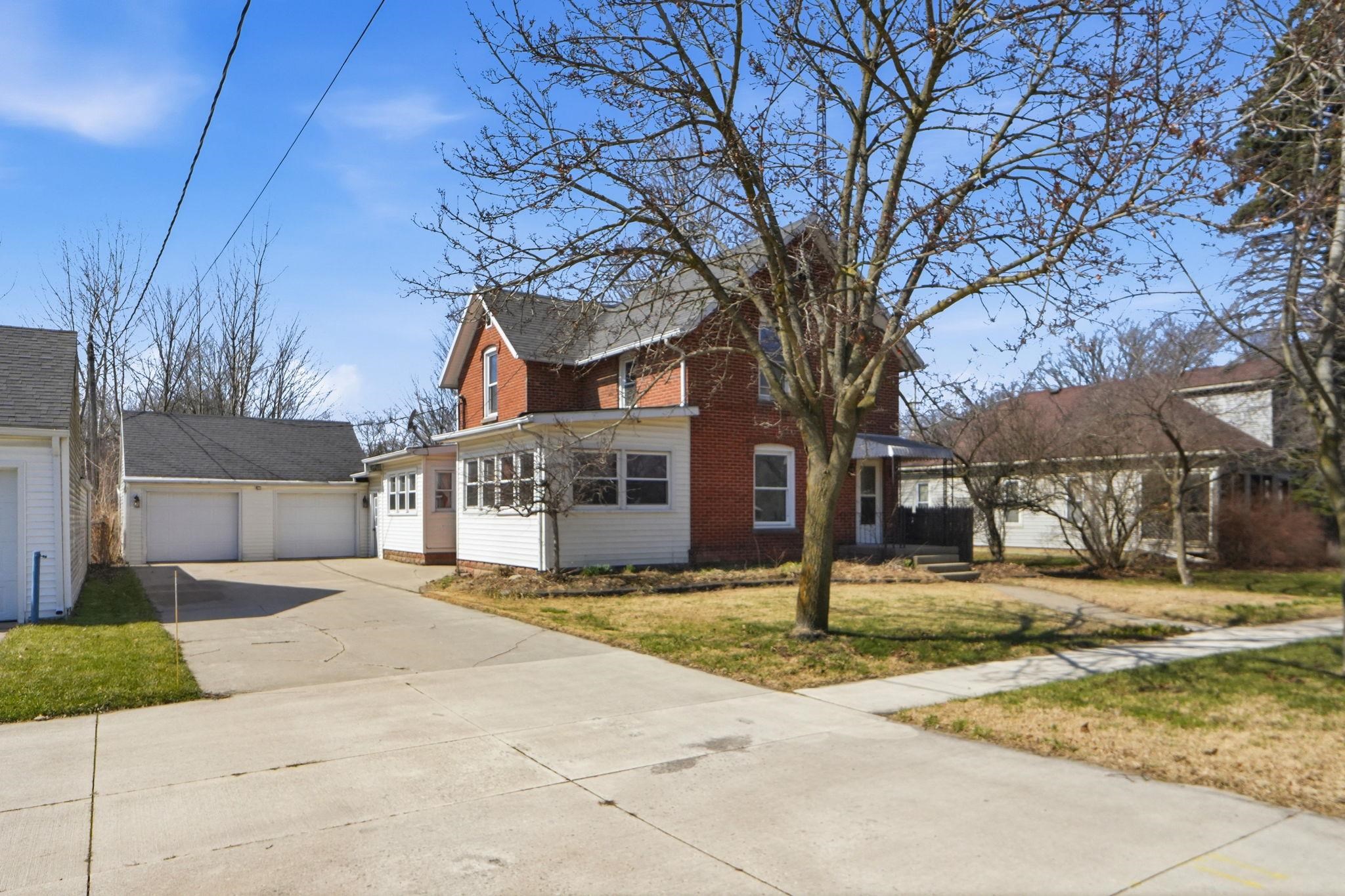 Traditional home featuring a front lawn, brick siding, covered porch, and a garage