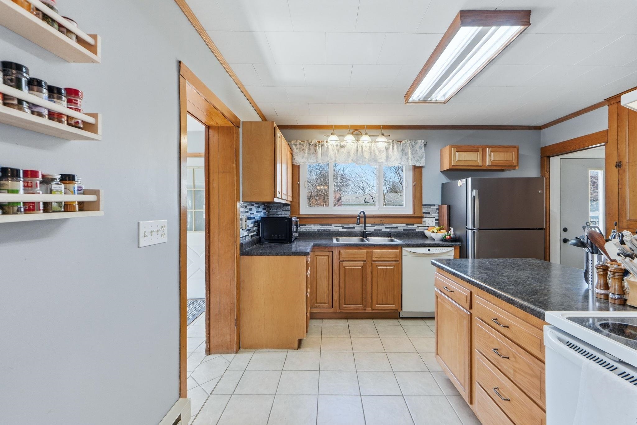 Kitchen with dark countertops, white appliances, light tile patterned floors, tasteful backsplash, and ornamental molding