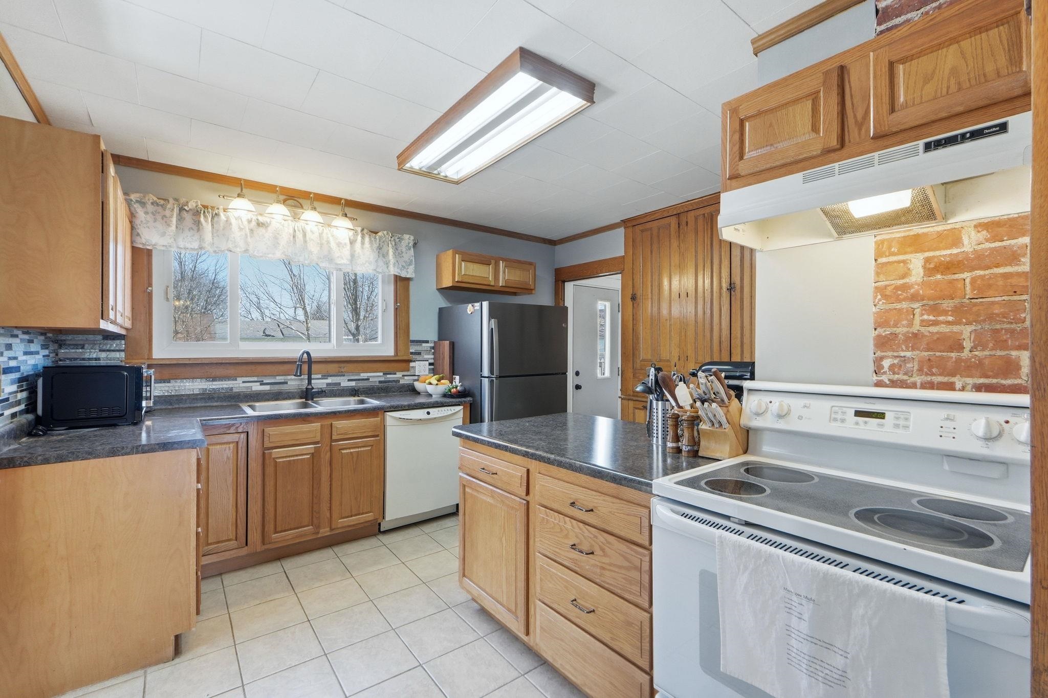 Kitchen with white appliances, dark countertops, ornamental molding, wood finish cabinetry, and light tile patterned flooring
