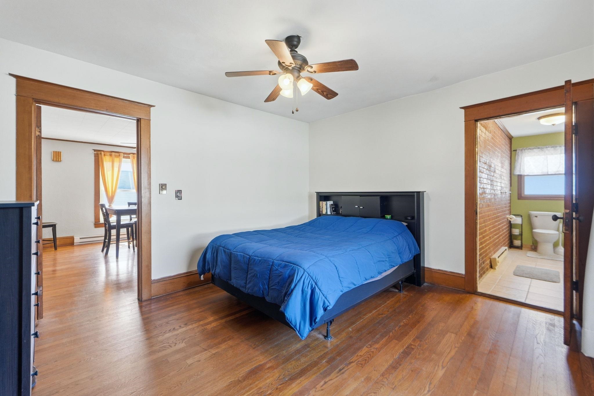 Bedroom featuring dark wood-style floors, ceiling fan, a baseboard radiator, ensuite bath, and a baseboard heating unit