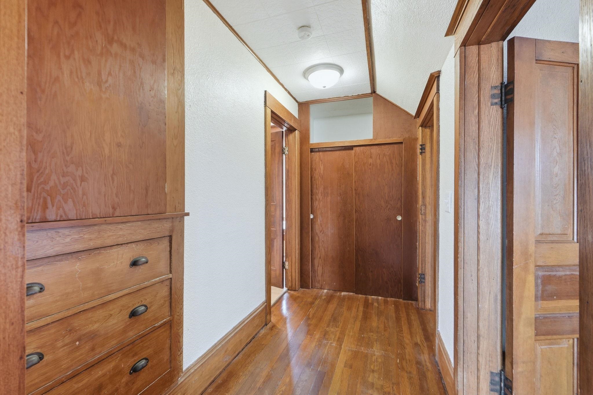 Corridor with a textured wall, hardwood / wood-style floors, and vaulted ceiling
