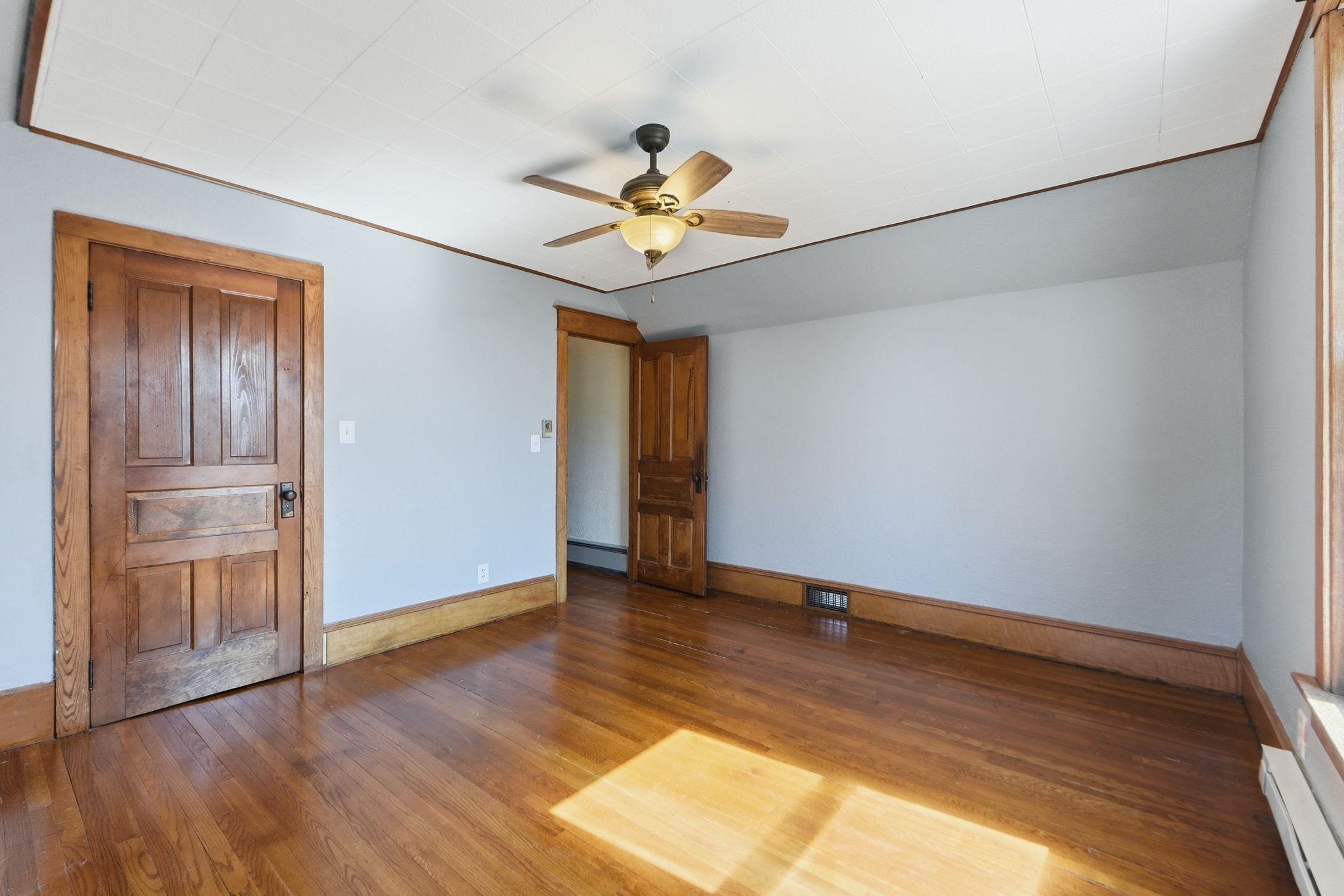 Unfurnished bedroom featuring hardwood / wood-style floors, baseboard heating, and ceiling fan