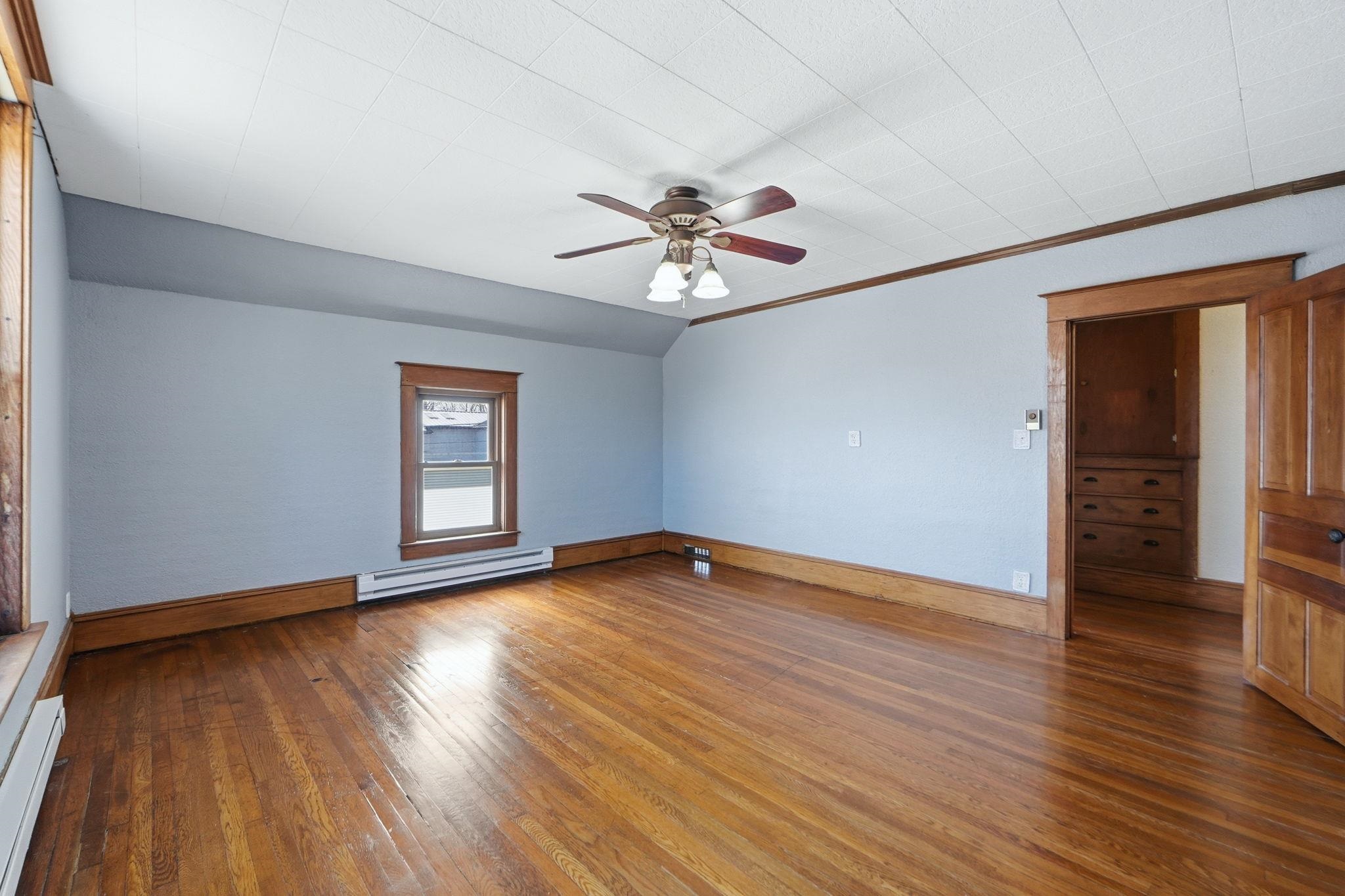 Unfurnished room featuring dark wood-style flooring, a ceiling fan, a baseboard radiator, baseboard heating, and vaulted ceiling