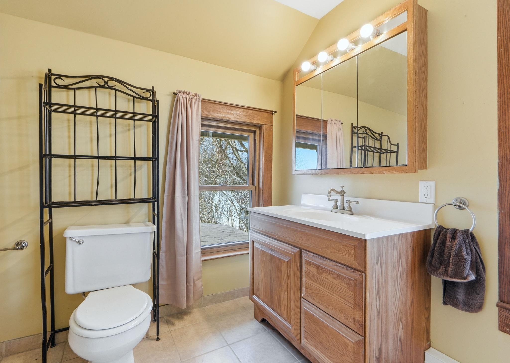 Full bath with vanity, light tile patterned floors, and lofted ceiling