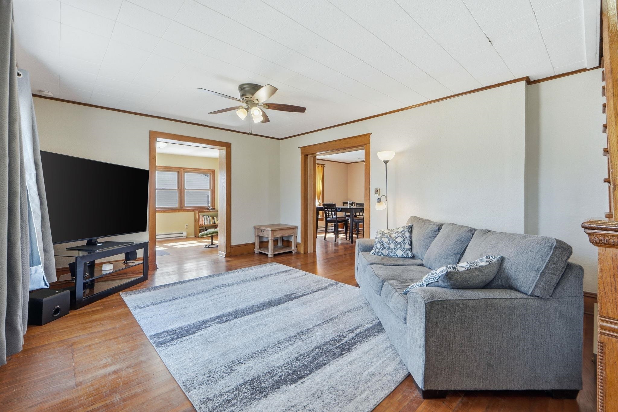 Living area with a ceiling fan, wood finished floors, ornamental molding, and a baseboard radiator